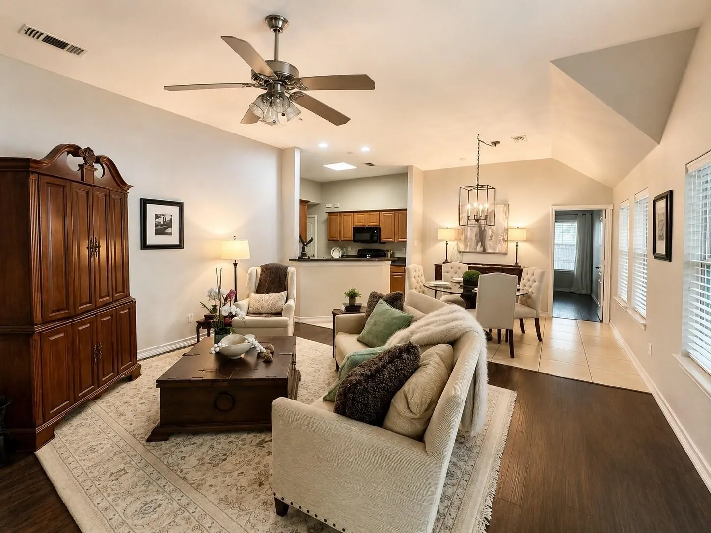 Open-concept living space featuring vaulted ceilings, a ceiling fan with integrated lighting, wood-finish flooring, and multiple windows with blinds