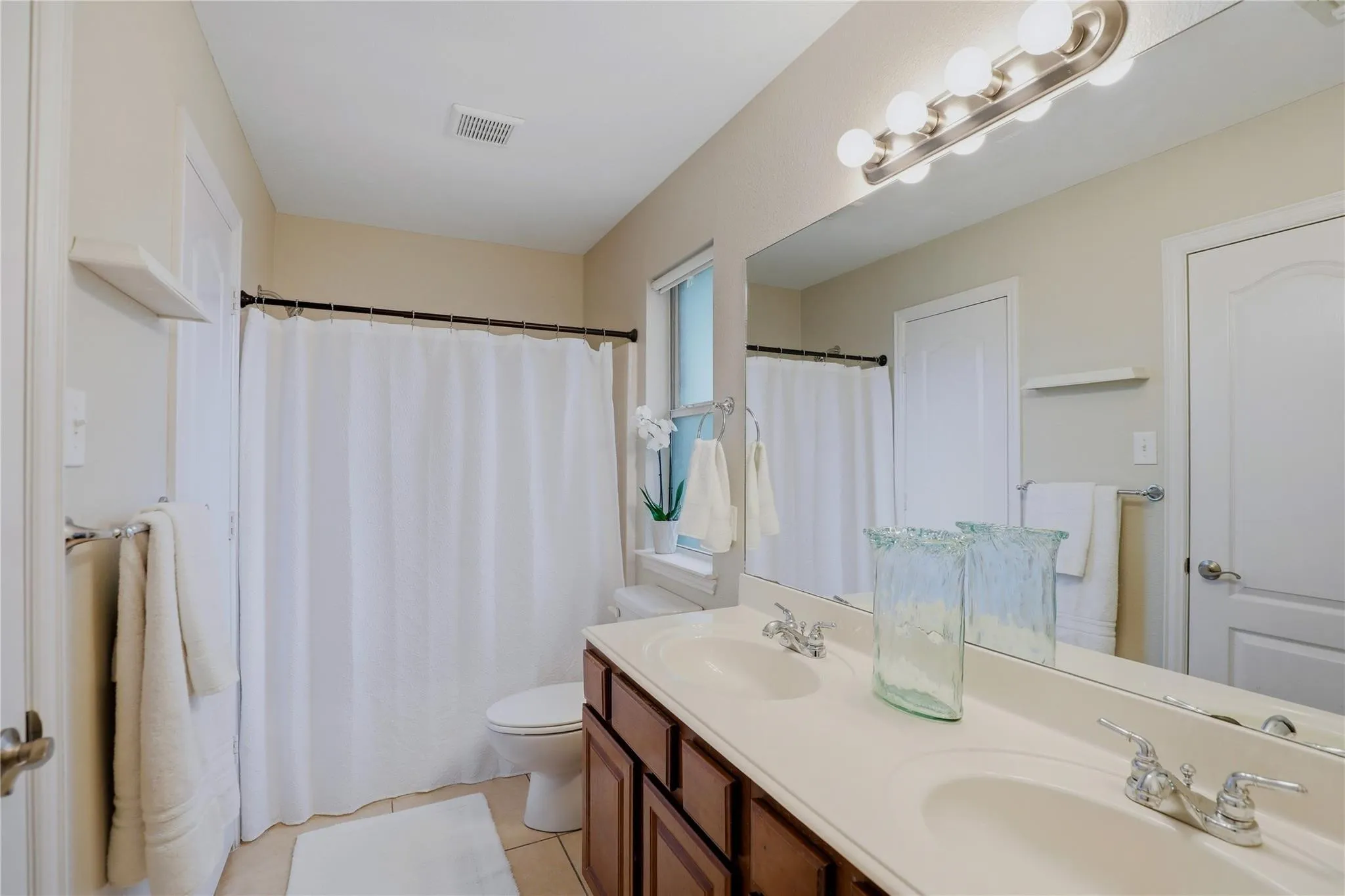 Dual vanity with integrated sinks, brushed nickel fixtures, wood-finish cabinetry, and a full-width mirror