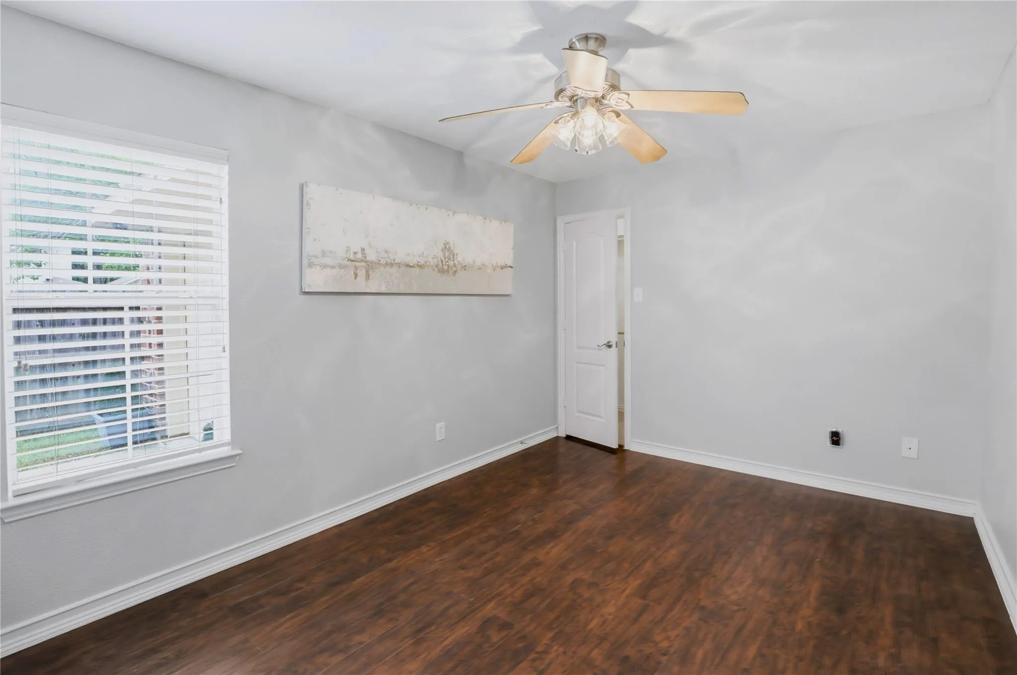 Wood-finish flooring, light gray walls, white trim, window with blinds, and ceiling fan with light fixture