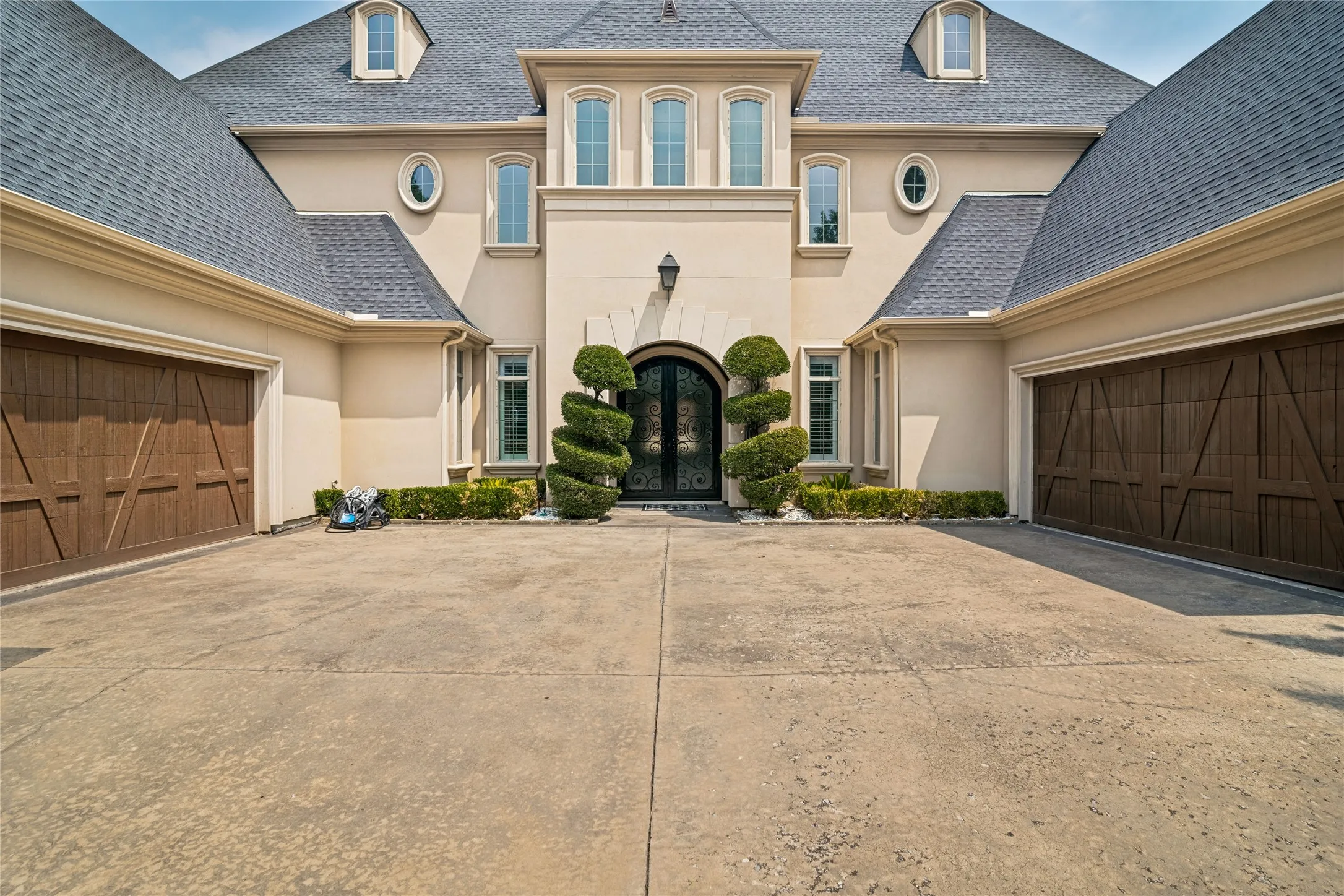 Stucco exterior with multiple dormer windows, a prominent arched entry, and two wood-finish garage doors