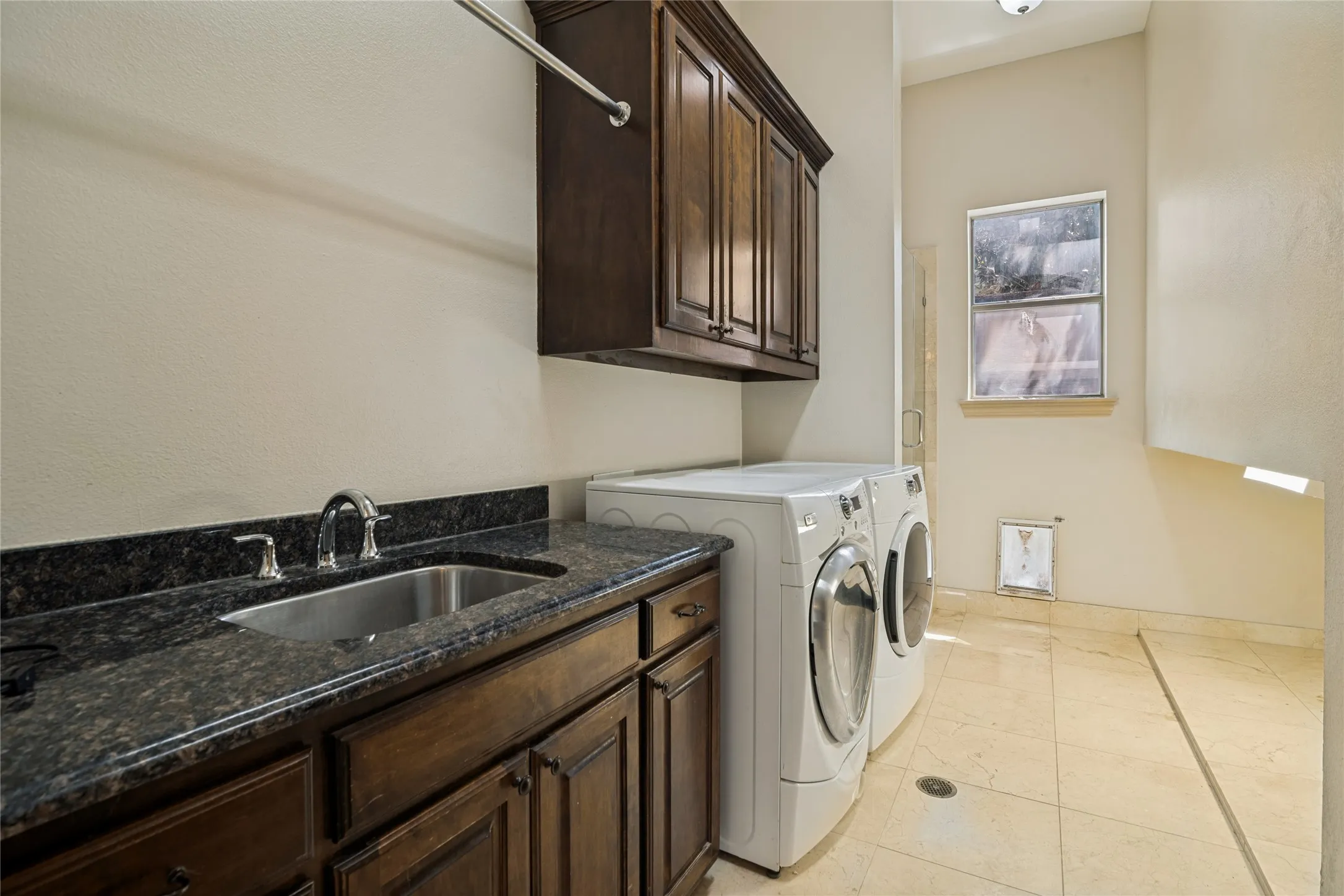 Laundry area featuring a built-in sink, dark wood cabinetry, and light-toned floor tiling