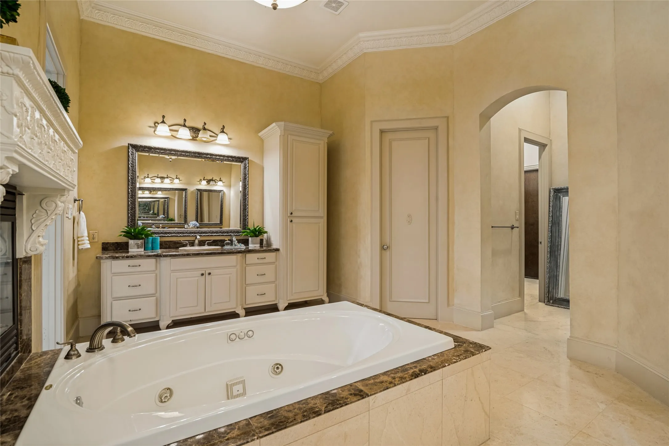 Jetted soaking tub with stone surround, dual vanity with undermount sinks, built-in cabinetry, and tile flooring