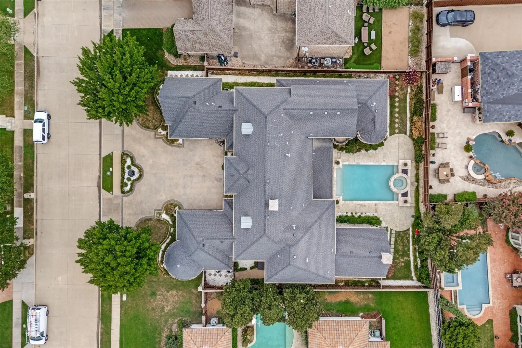Expansive property featuring a multi-gabled roofline, a large swimming pool with an integrated spa, and a circular driveway with a central landscaped island