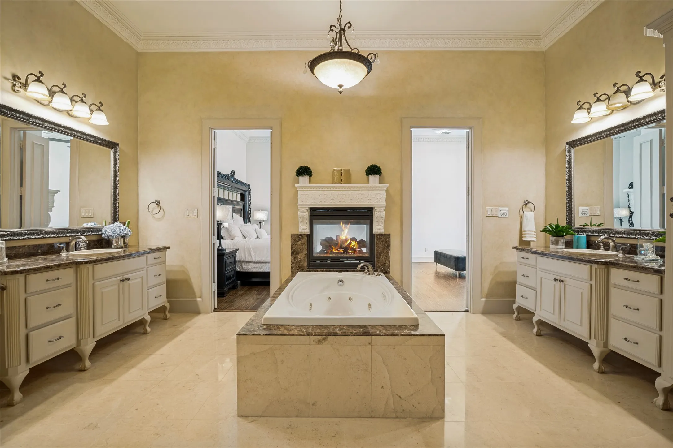Dual vanity sinks with granite countertops, built-in jetted tub, central fireplace, and tile flooring
