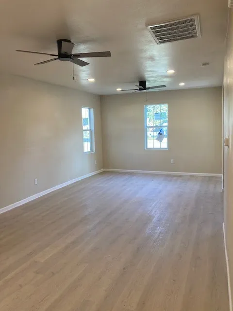 Expansive room featuring wood-finish flooring, two ceiling fans, recessed lighting, and multiple windows