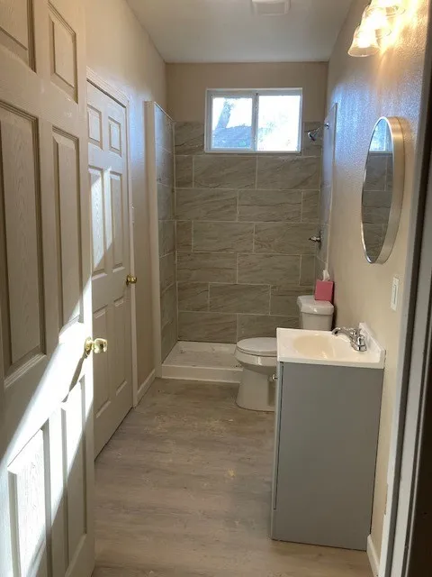 Bathroom featuring wood-finish flooring, a contemporary vanity with an integrated sink, and a tiled shower surround