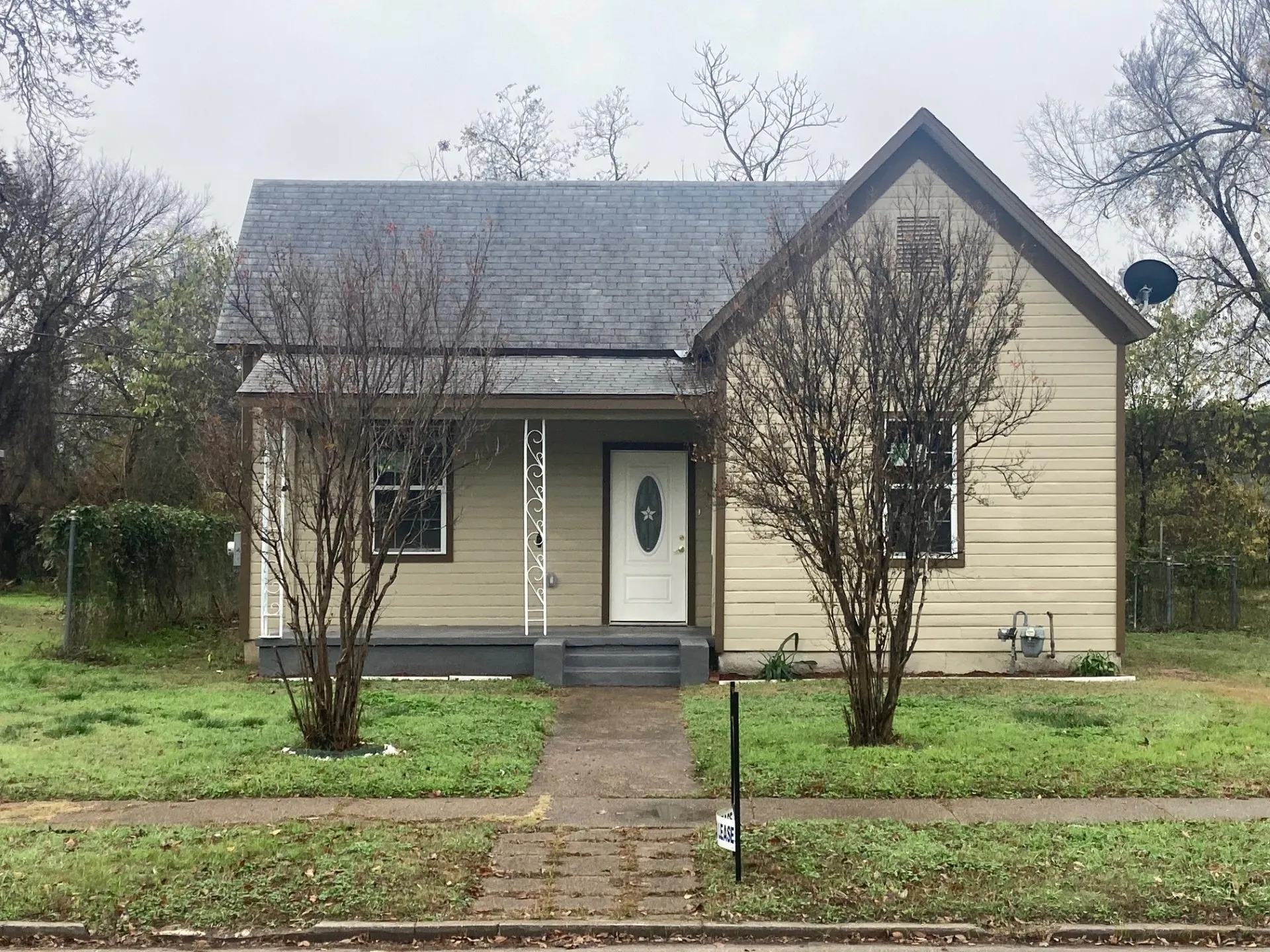 Single-story residence featuring light-colored siding, a dark-toned gable roof, and a front porch with decorative white columns