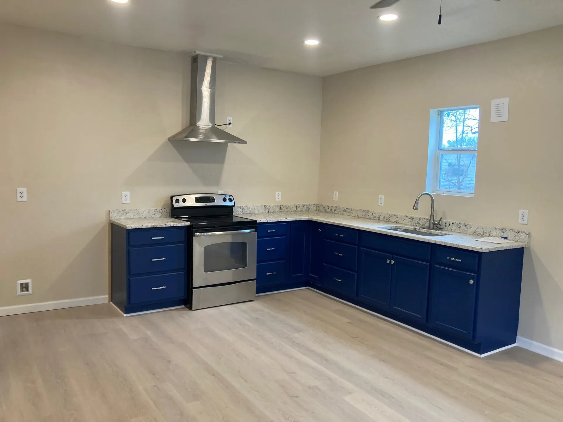 L-shaped kitchen featuring blue cabinetry, light-toned countertops, and stainless steel appliances including a range with an overhead vent hood