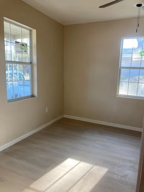 Neutral tone wall finishes, two windows with gridded panes, wood-finish flooring, and a ceiling fan