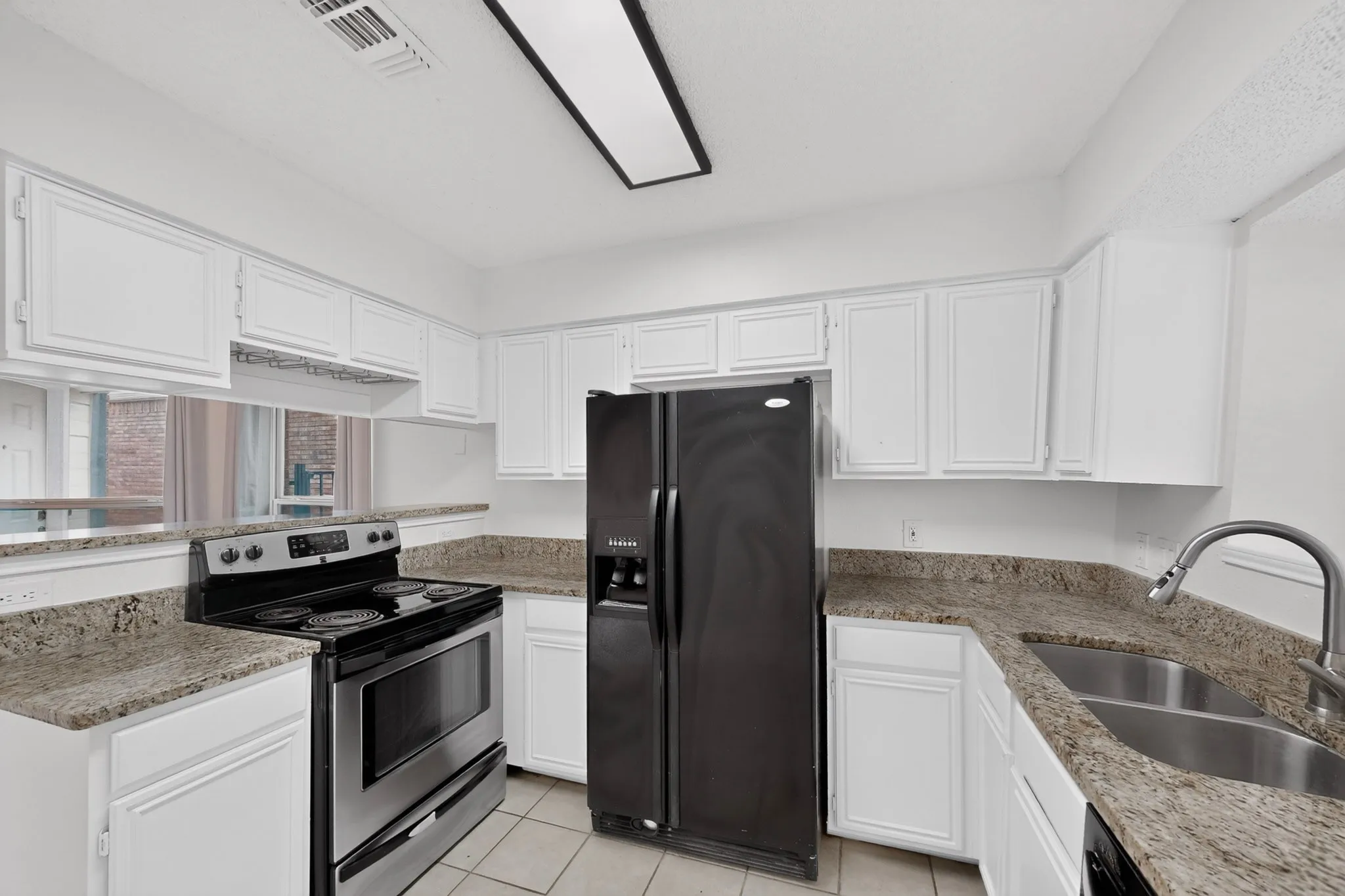 Kitchen featuring white cabinetry, granite-style countertops, a dual basin stainless steel sink, and a black side-by-side refrigerator