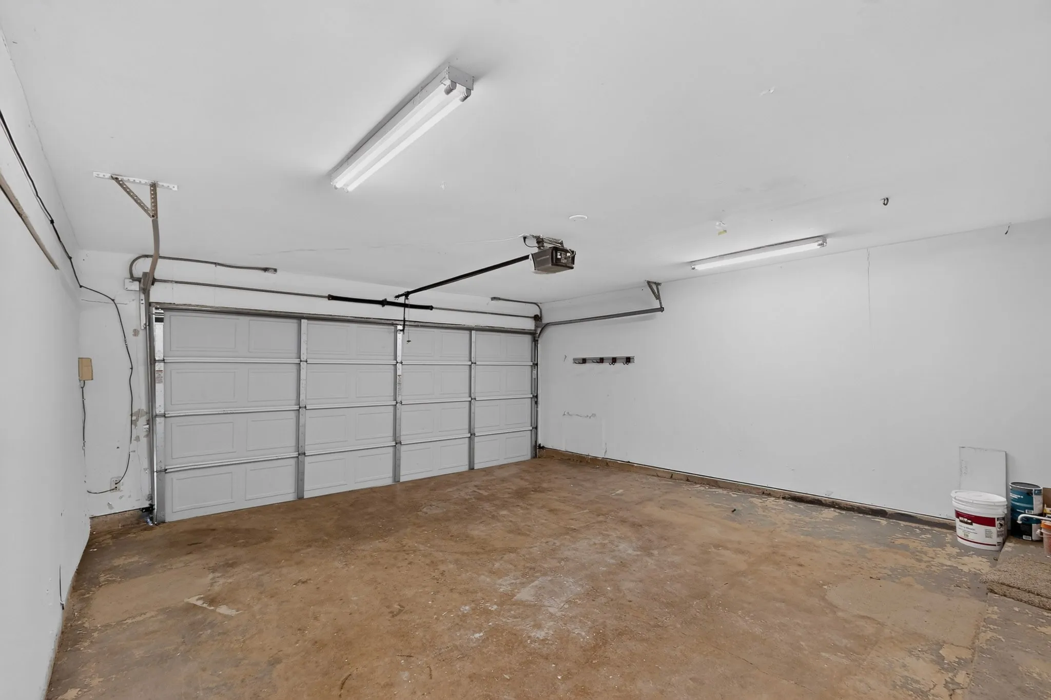 Attached garage featuring a white paneled door, exposed ceiling-mounted track, and fluorescent lighting