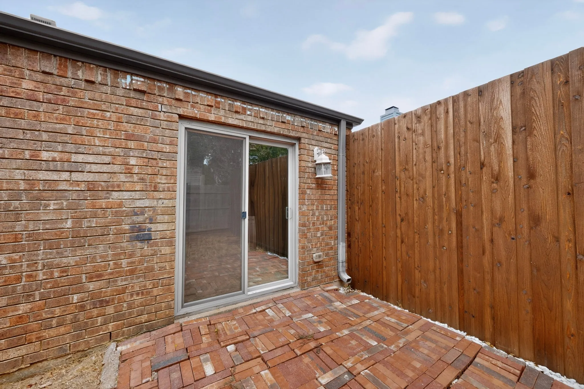 Brick exterior with a privacy fence, sliding glass door, and brick paver patio