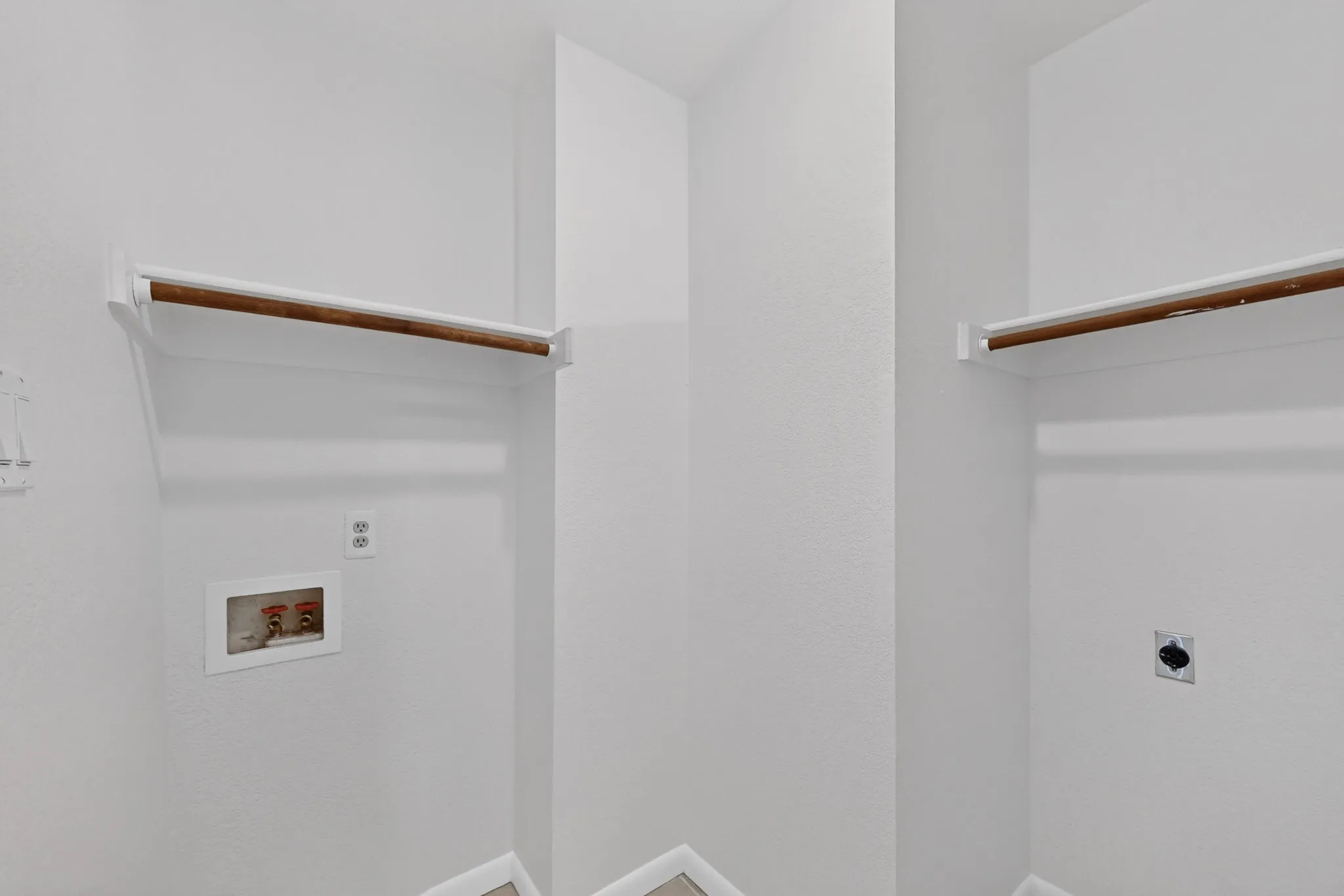 Laundry area with overhead shelving, wood-finish hanging rods, utility hookups, and neutral wall finishes