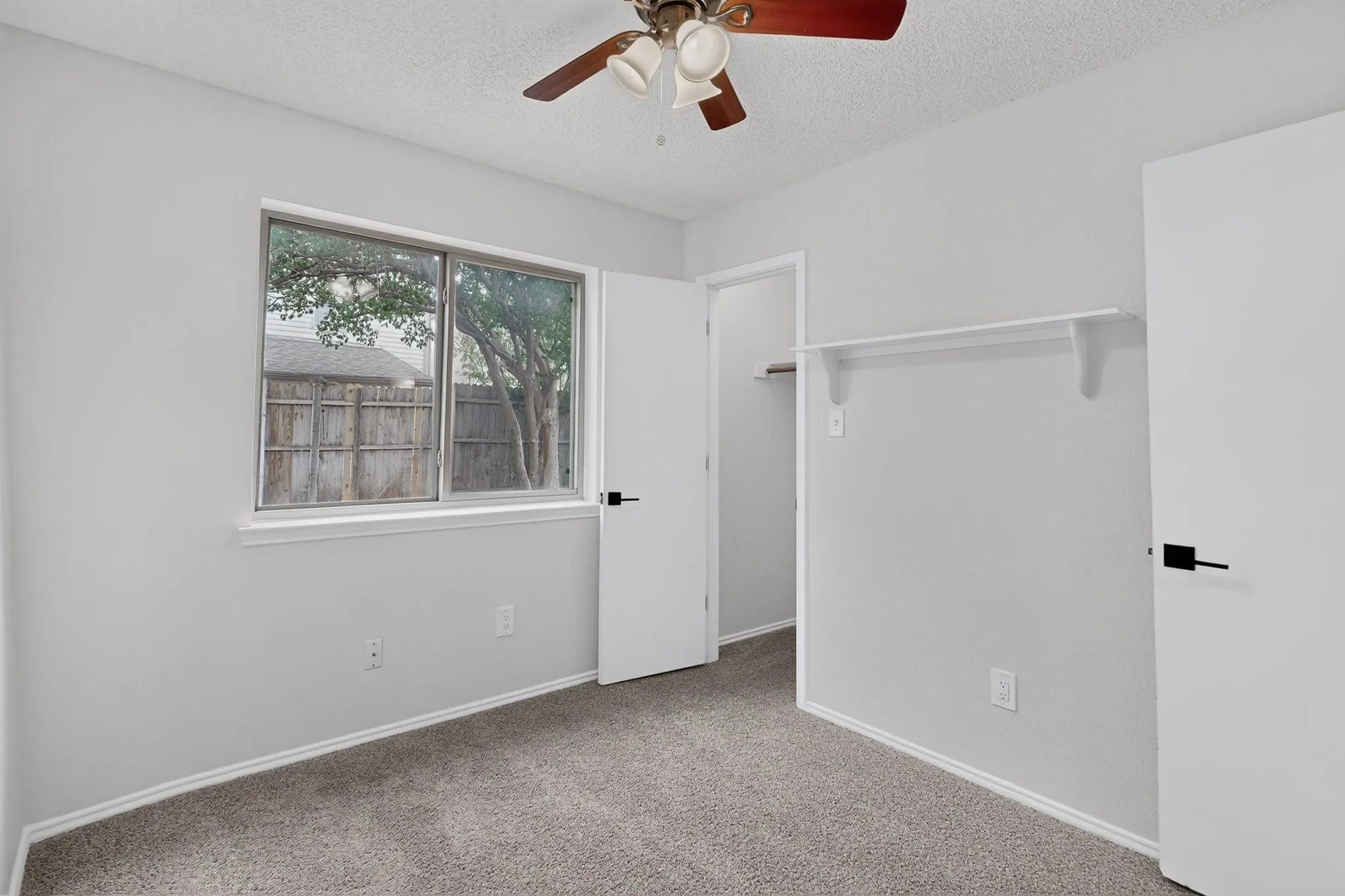 Neutral wall paint with carpet flooring, a window offering natural light, and a built-in closet shelf