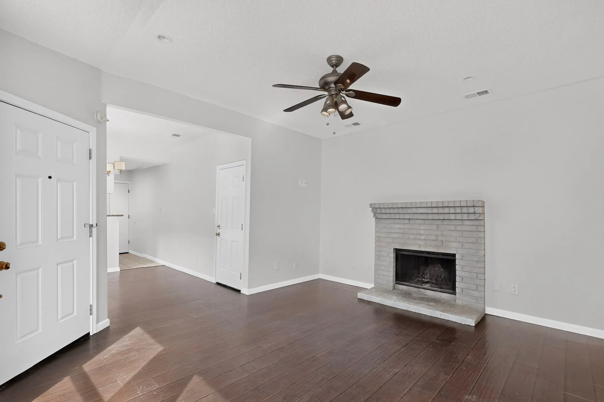 Wood-finish flooring, brick fireplace, ceiling fan with light fixture, and white interior doors