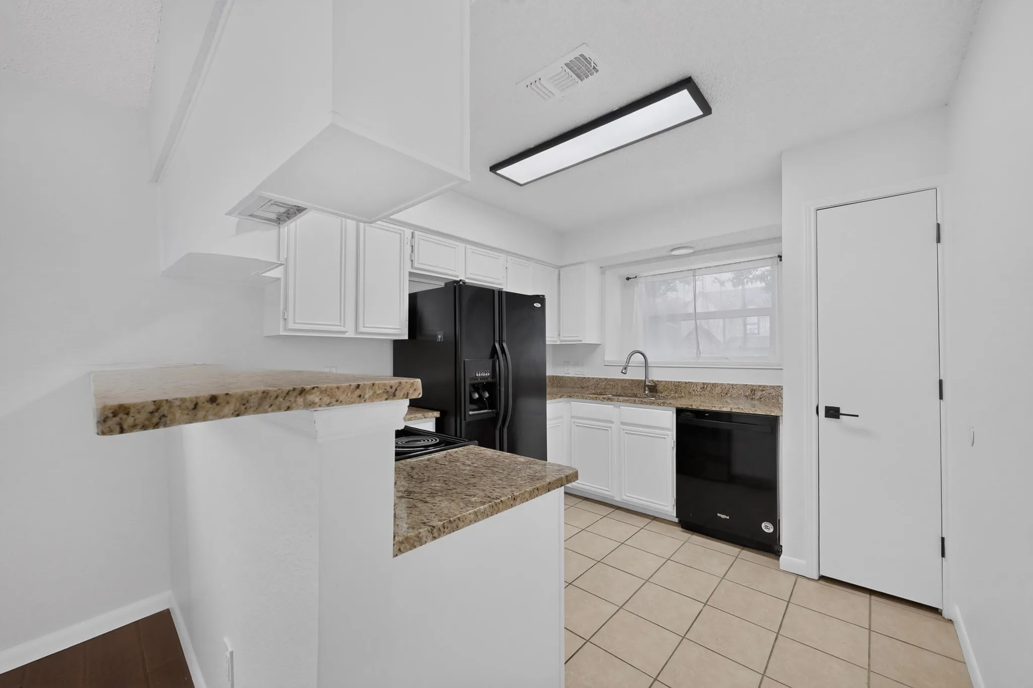 Kitchen featuring white cabinetry, light-toned countertop, tile flooring, and black appliances