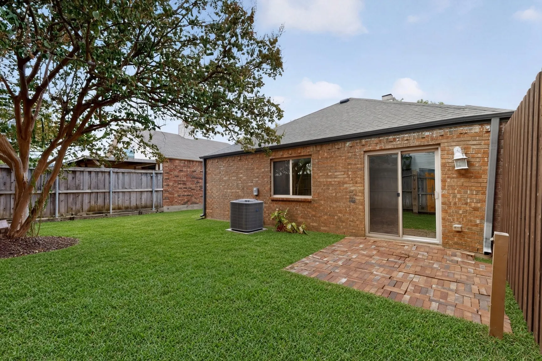 Expansive green lawn, mature tree, brick exterior, sliding glass door, and paver patio - AI enhanced