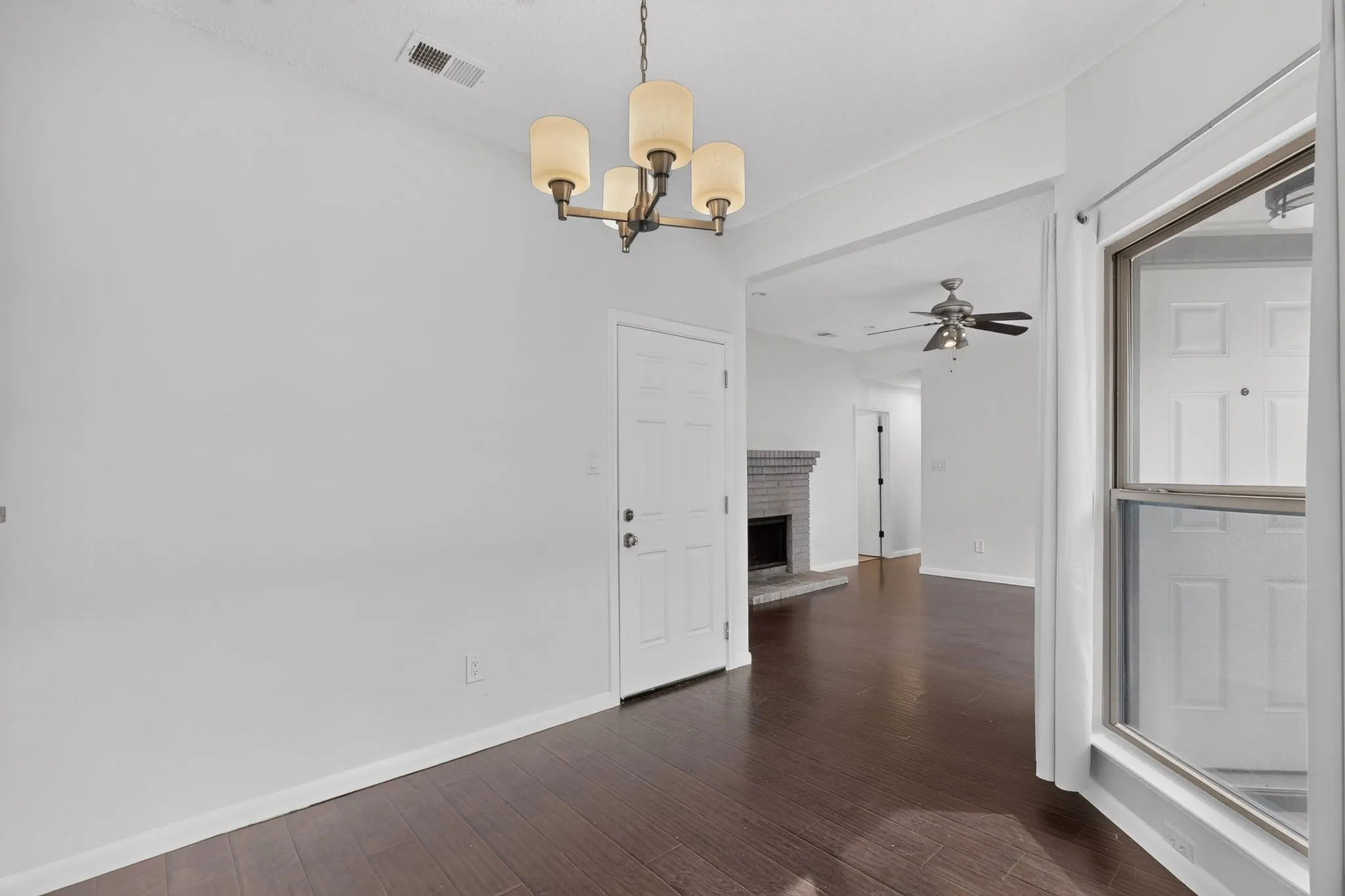 Vaulted ceiling with an attached light fixture, white interior door, dark wood-finish flooring, and a window with white trim