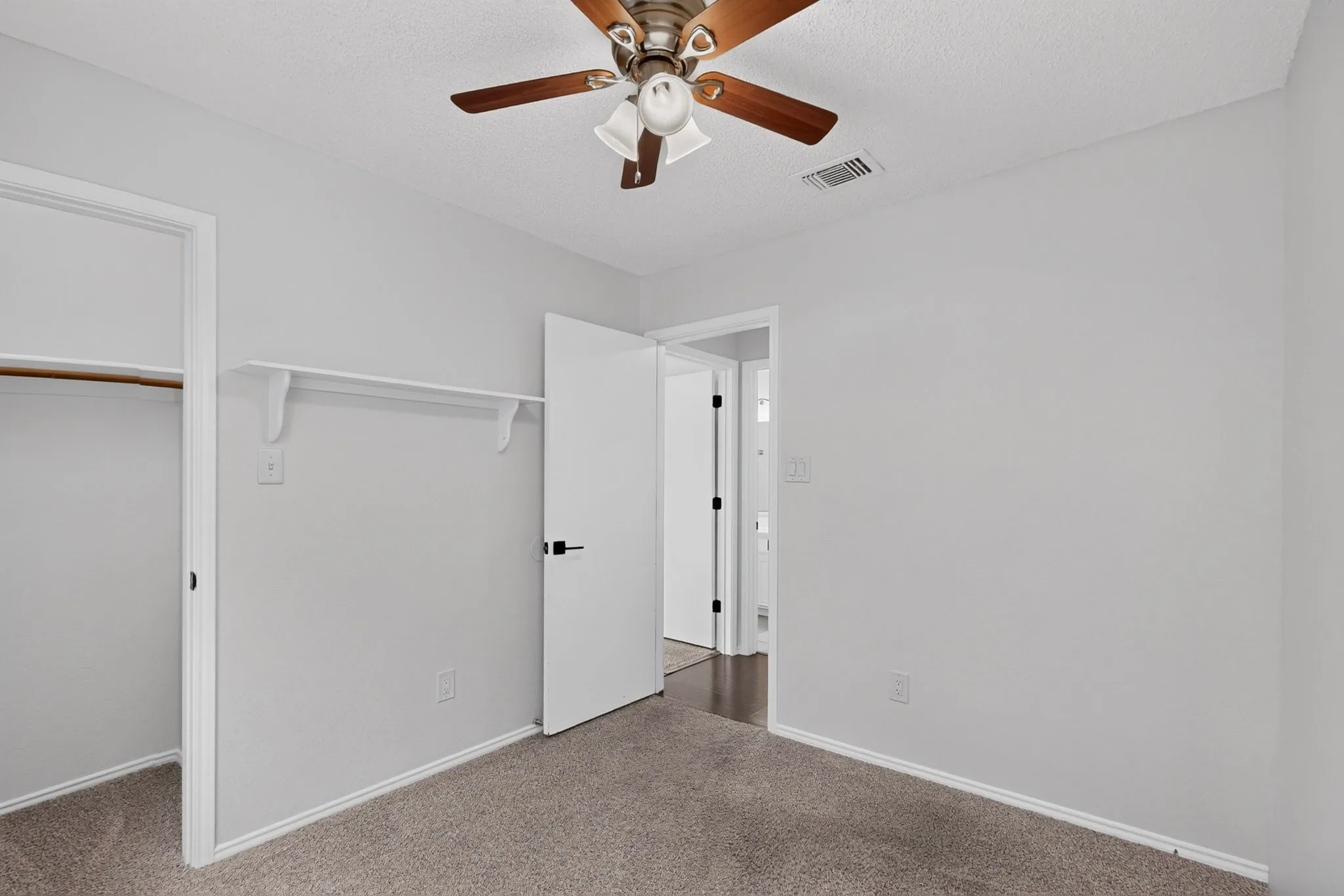 Neutral wall paint, ceiling fan with light fixture, carpet flooring, open closet with hanging rod, and wall-mounted shelving