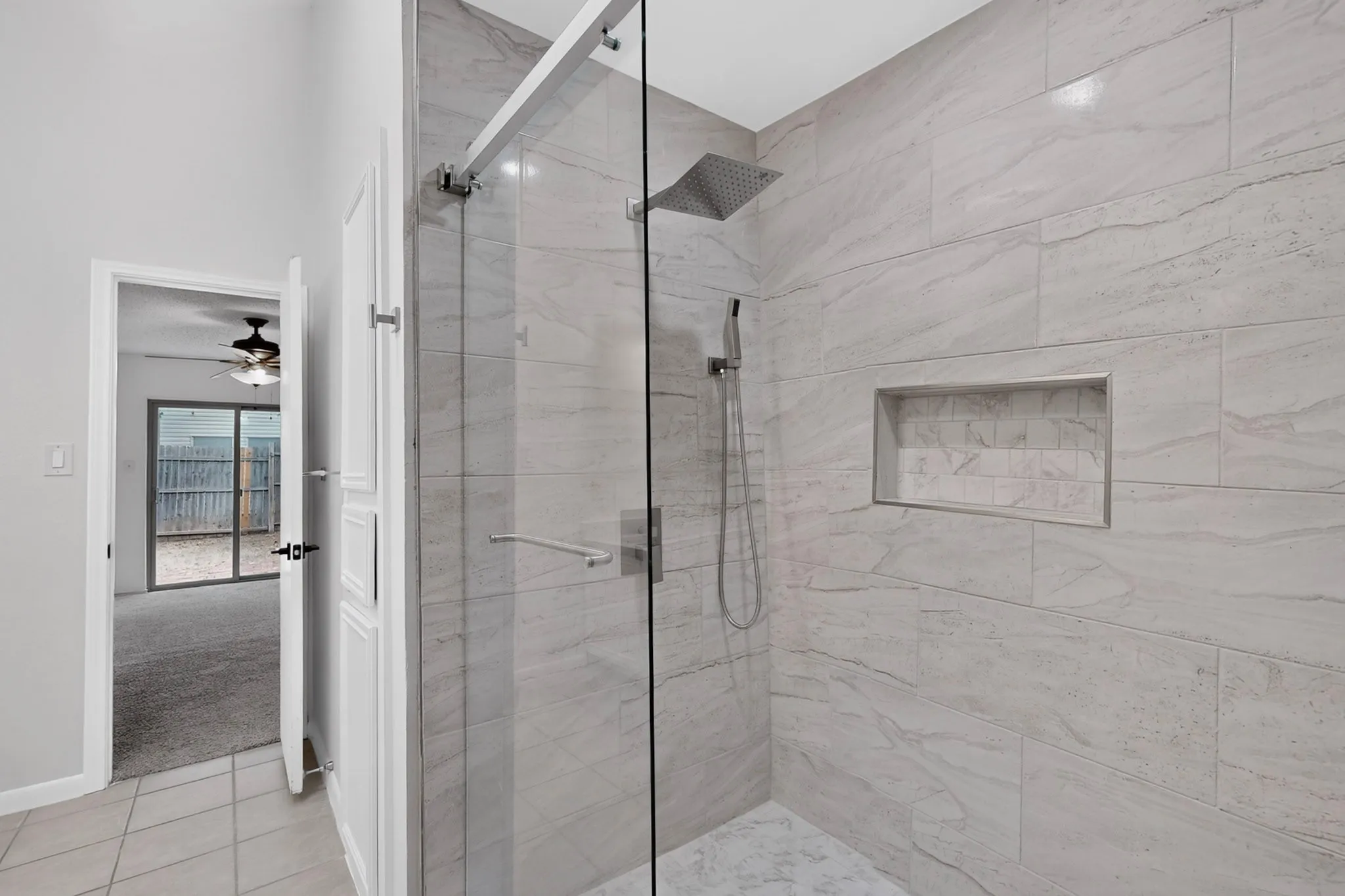 Glass-enclosed shower with large format wall tile, rain shower head, hand-held shower fixture, and recessed niche