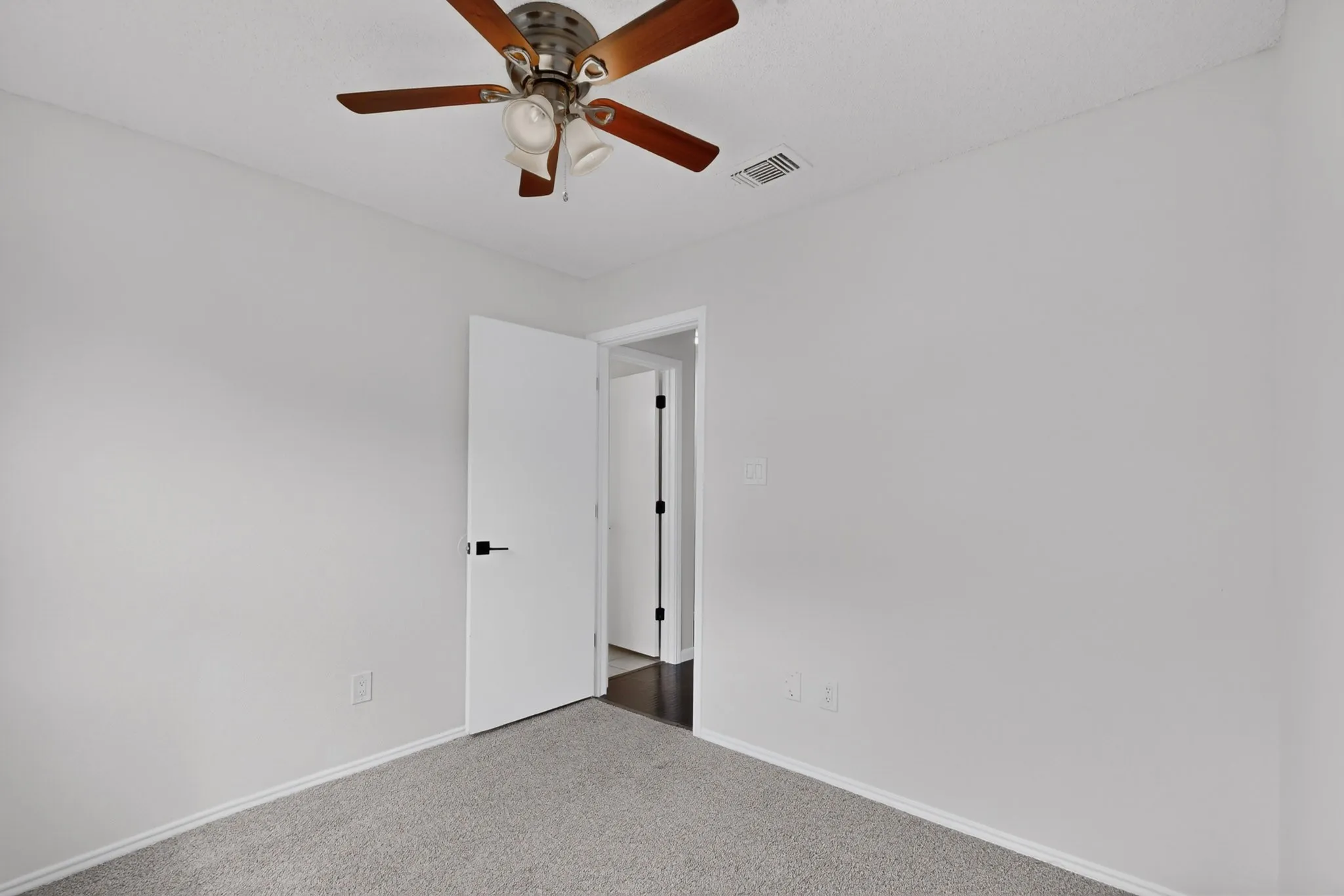 Ceiling fan with light fixture, light gray wall paint, gray carpet flooring, white door, and dark door hardware