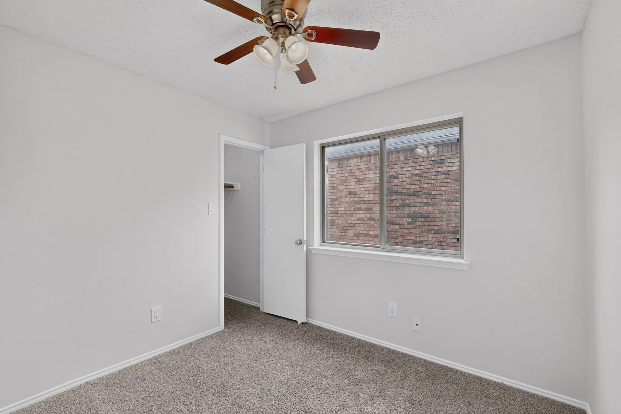 Neutral wall color, carpeted flooring, ceiling fan with integrated lighting, and a window for natural illumination