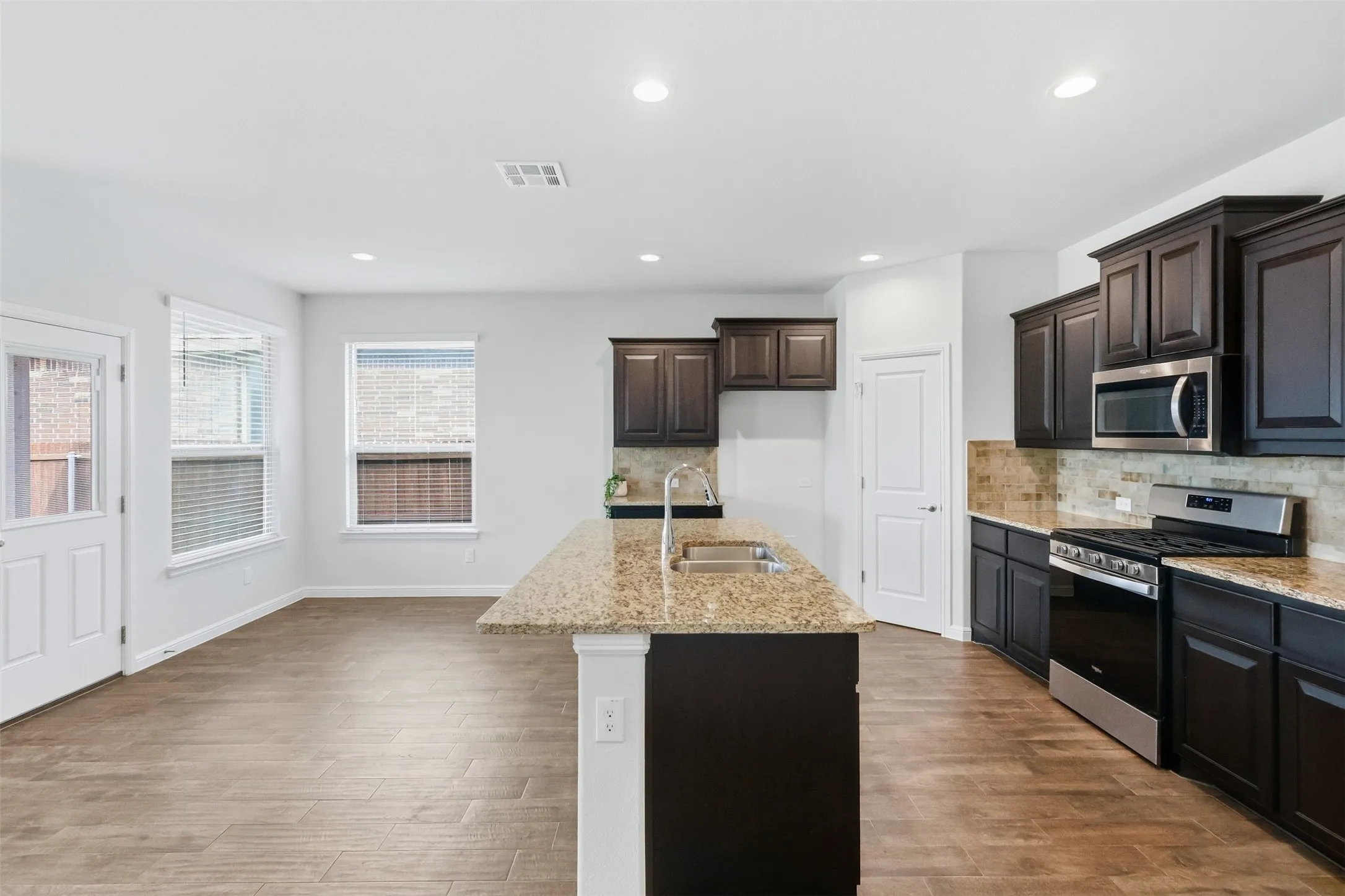 Kitchen featuring dark wood-finish cabinetry, stainless steel appliances, granite countertops, and a full-height tile backsplash