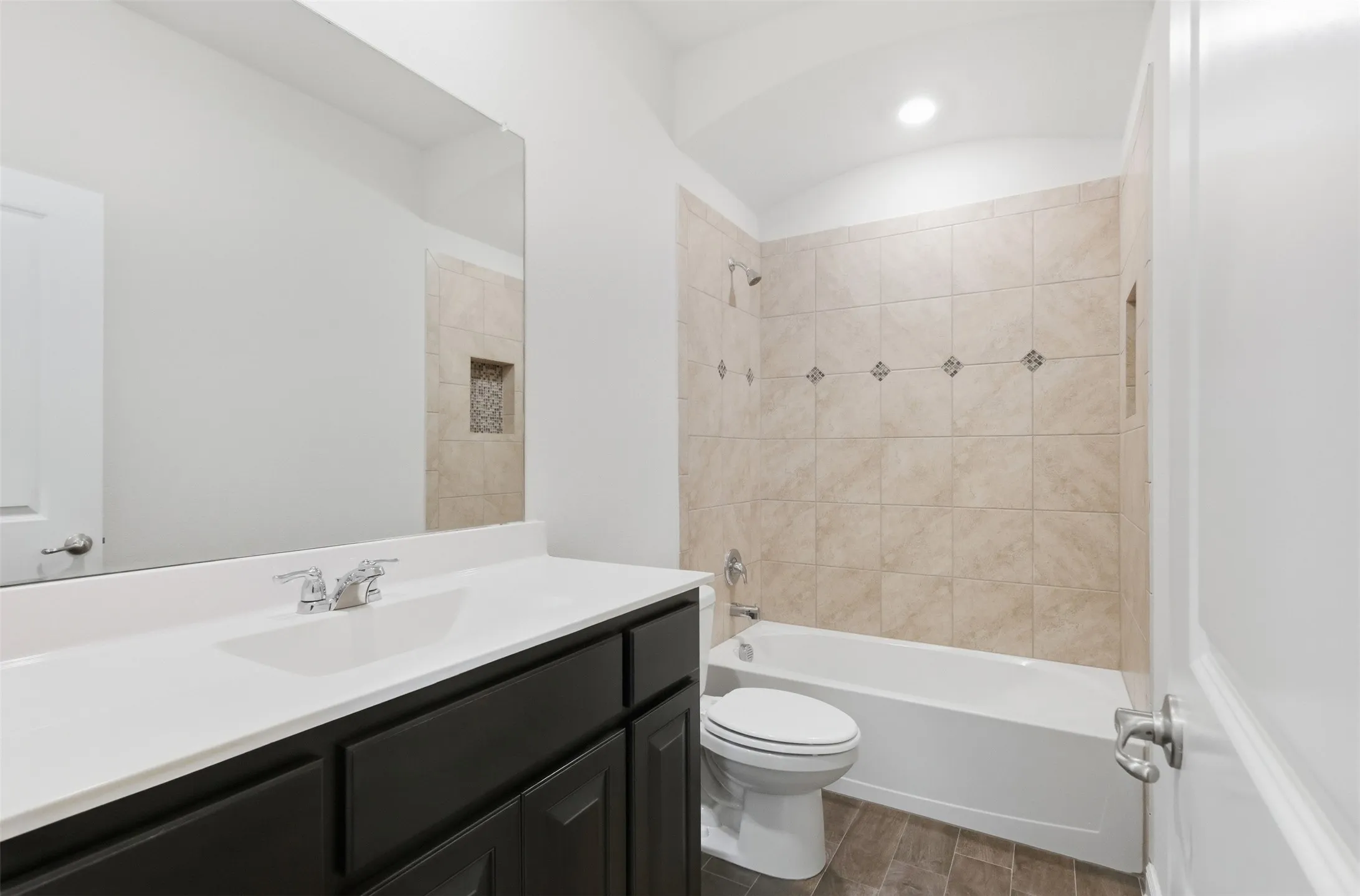 White vanity with a rectangular undermount sink, a large mirror, and a tiled shower-tub combination