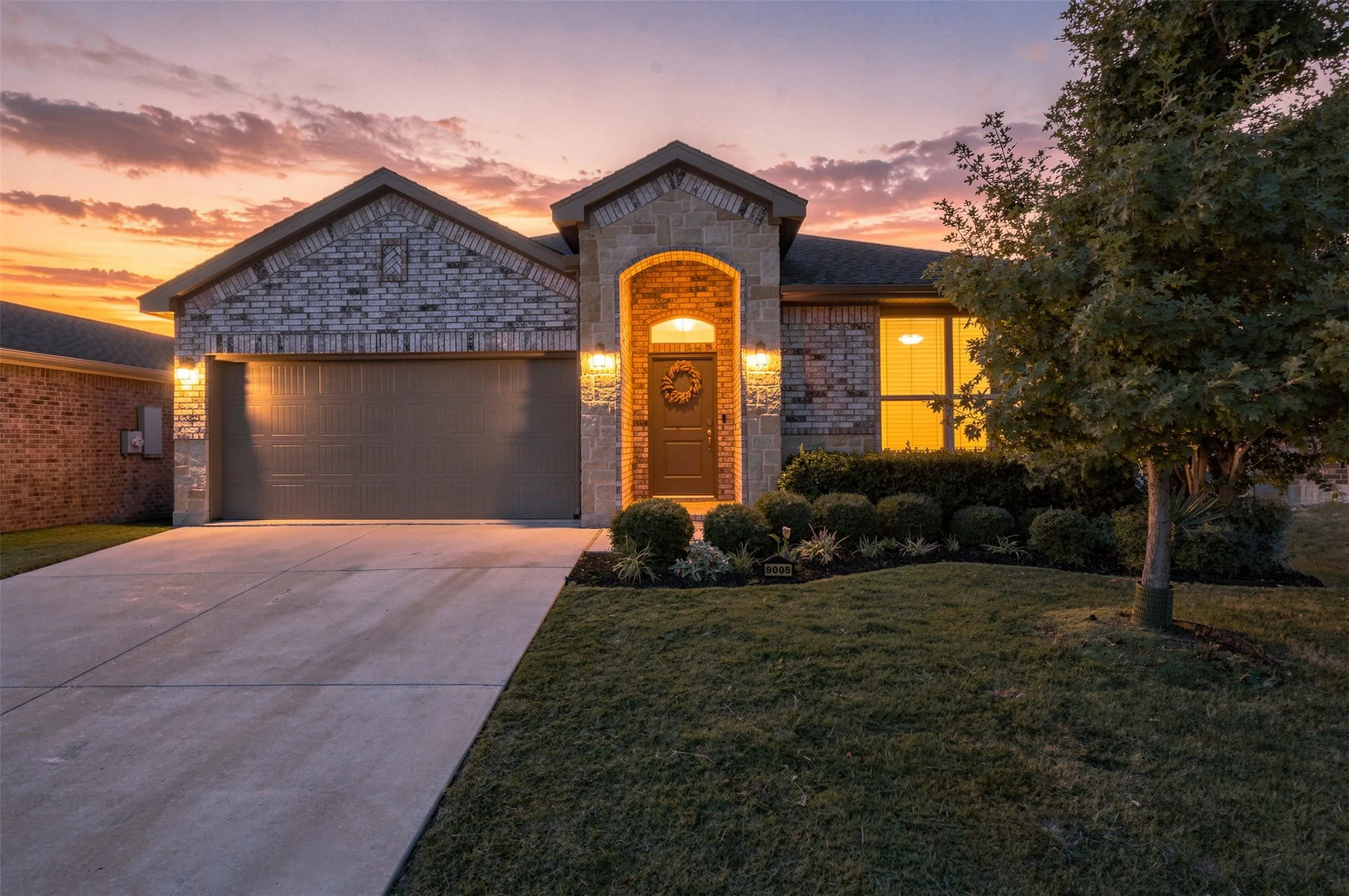 Brick and stone facade, arched entryway, two-car garage, concrete driveway, and established landscaping