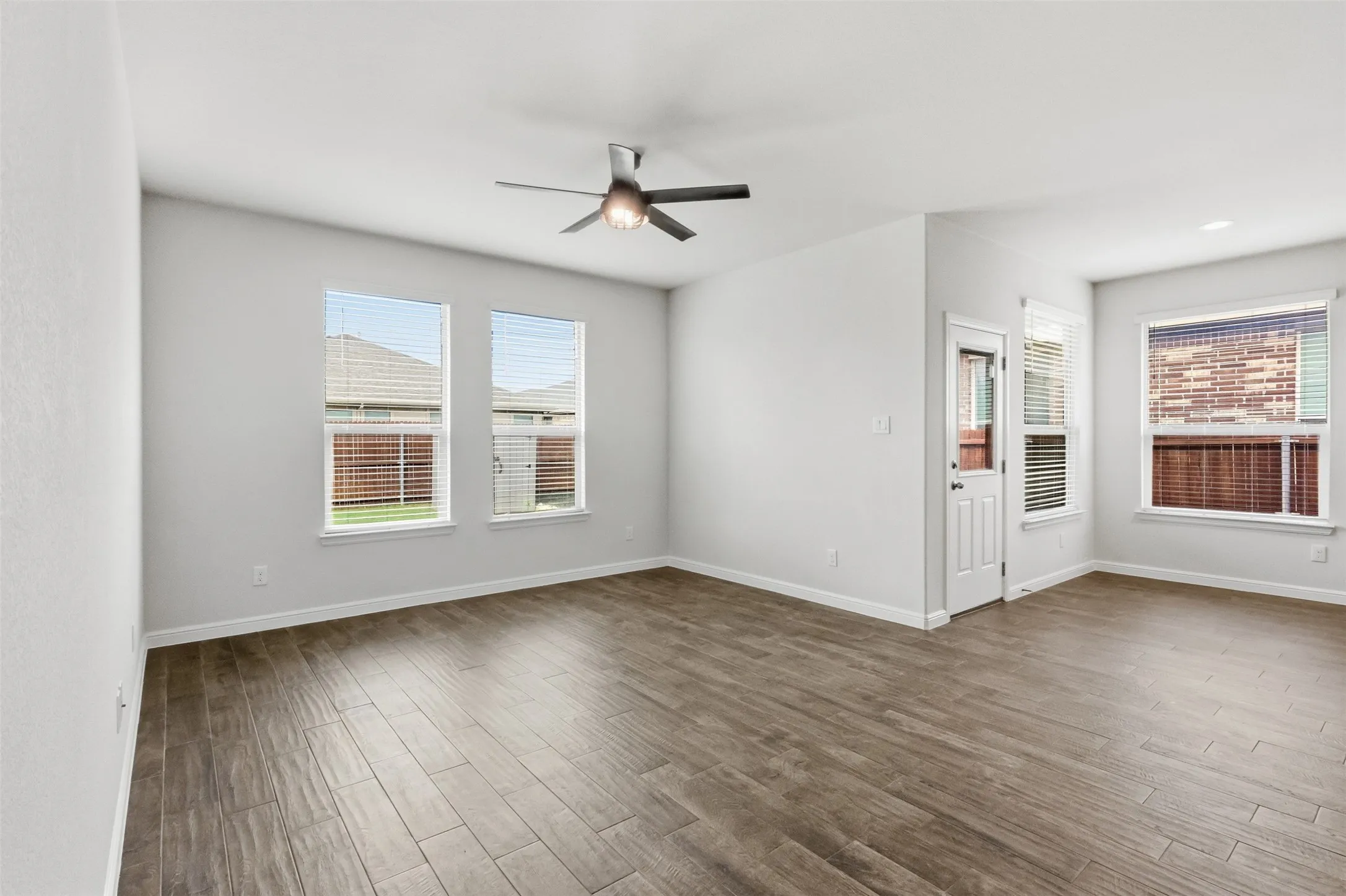 Spacious room featuring Tile flooring, multiple windows with blinds, a ceiling fan with integrated lighting, and a white paneled door