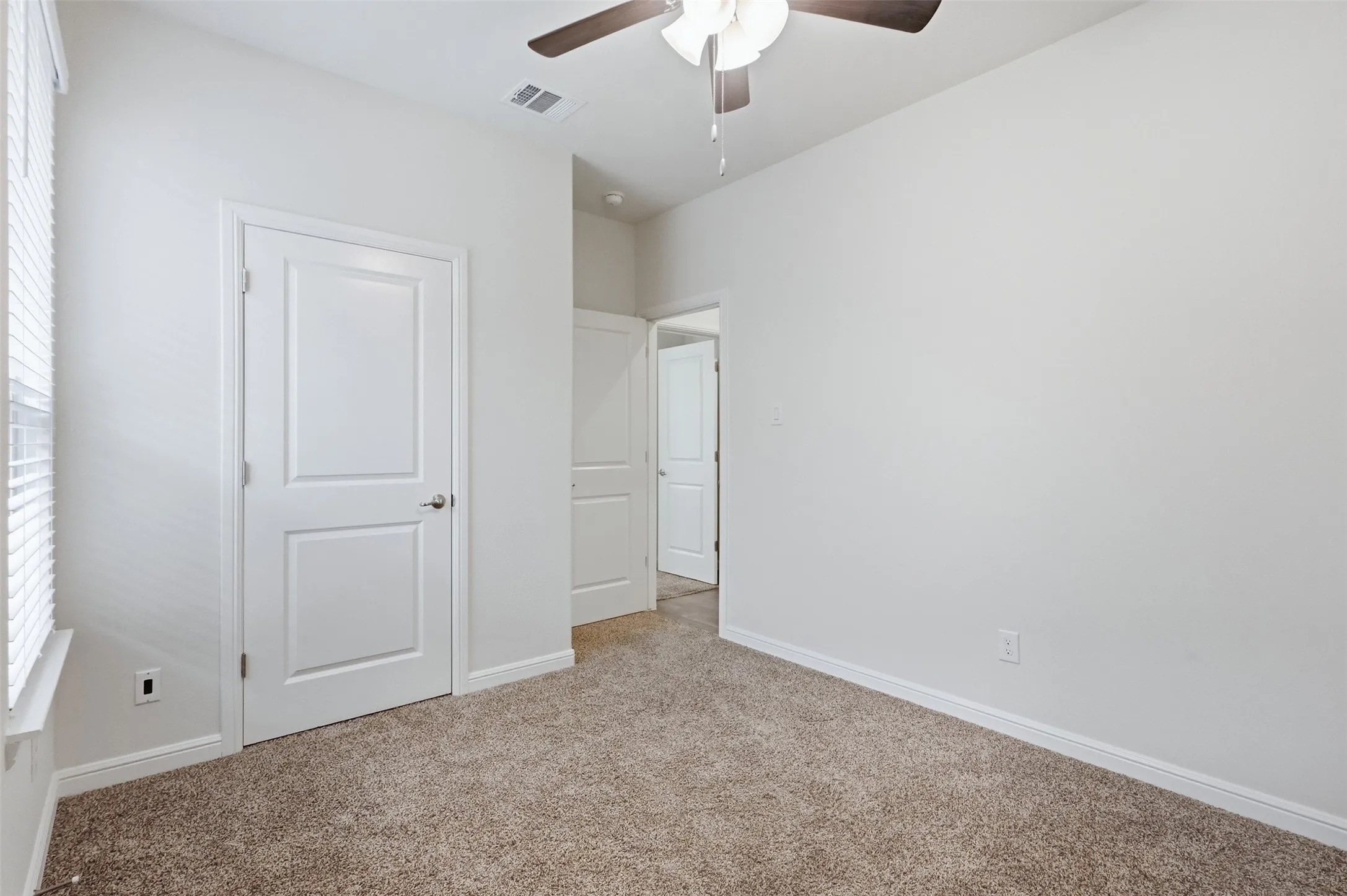 Neutral wall finishes, textured carpet flooring, ceiling fan with integrated lighting, and white interior doors