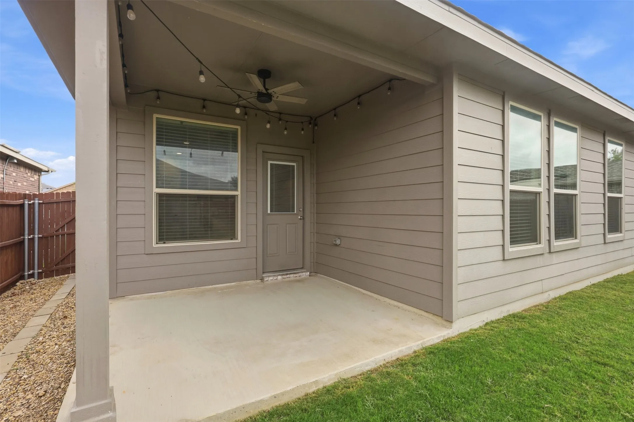 Covered patio with concrete flooring, equipped with a ceiling fan and string lighting