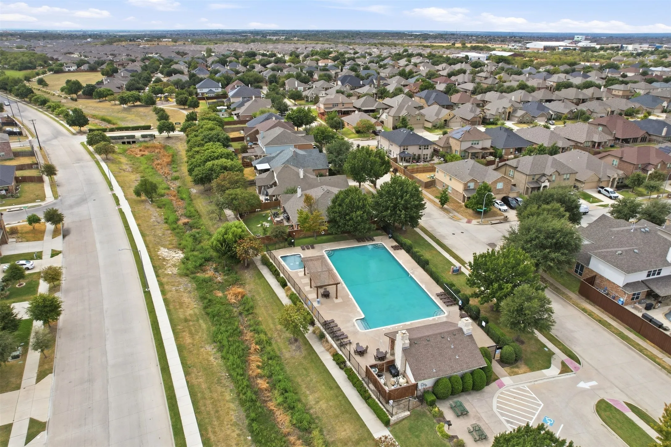 Community pool, spa, and amenity building with paved pool deck, shaded lounge areas, and perimeter fencing