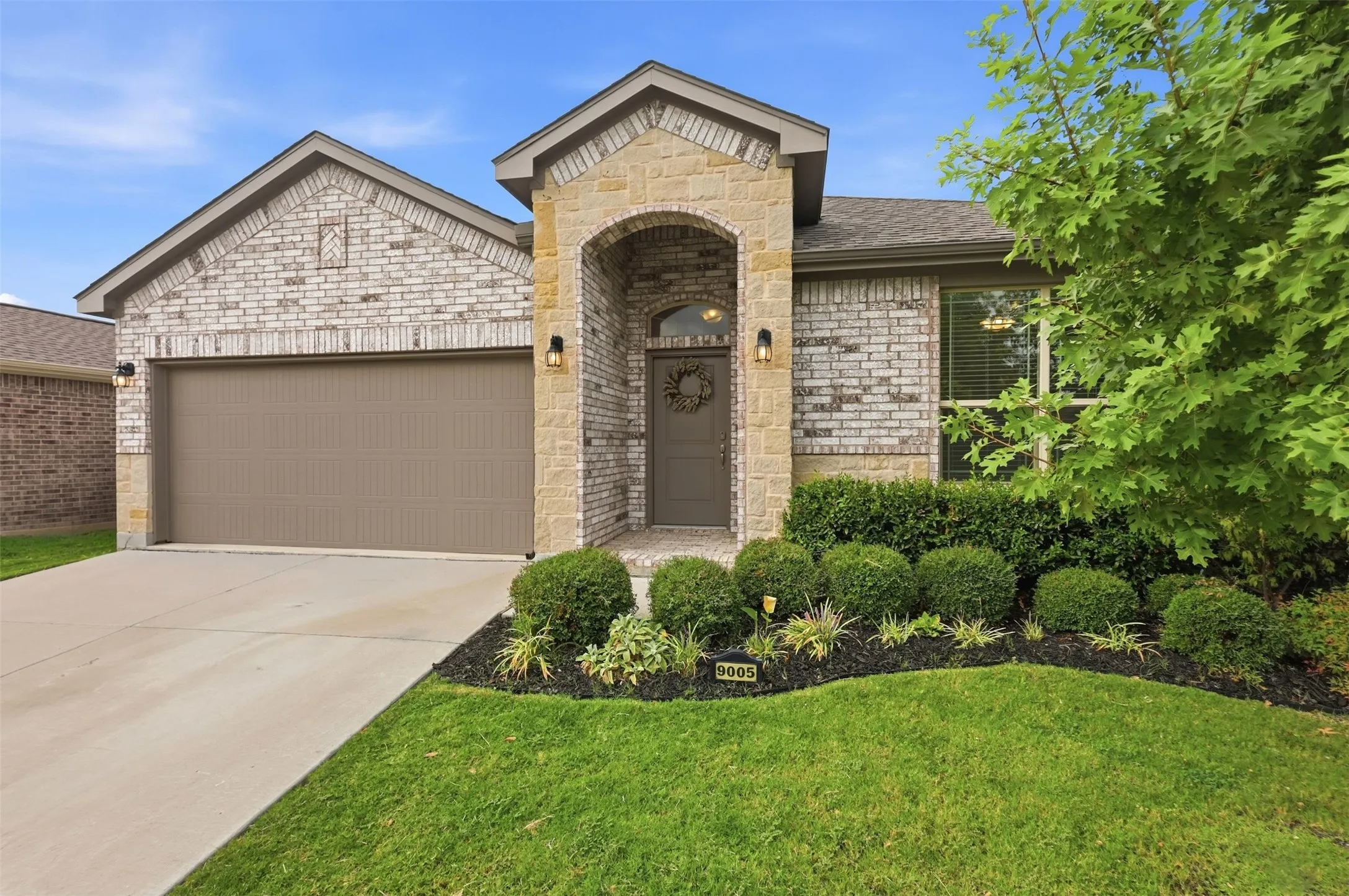 Brick and stone facade, arched entry, integrated two-car garage, mature landscaping, and concrete driveway