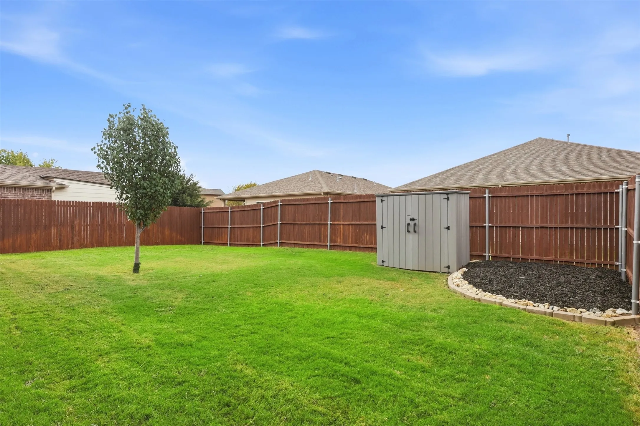 Expansive fenced backyard with a manicured lawn, a mature tree, and a storage shed