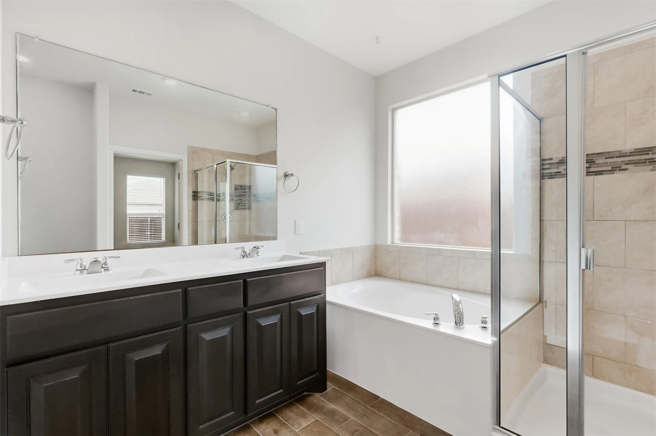 Dual sink vanity with dark wood-finish cabinetry, a framed mirror, a built-in tub, and a glass-enclosed shower featuring tiled walls