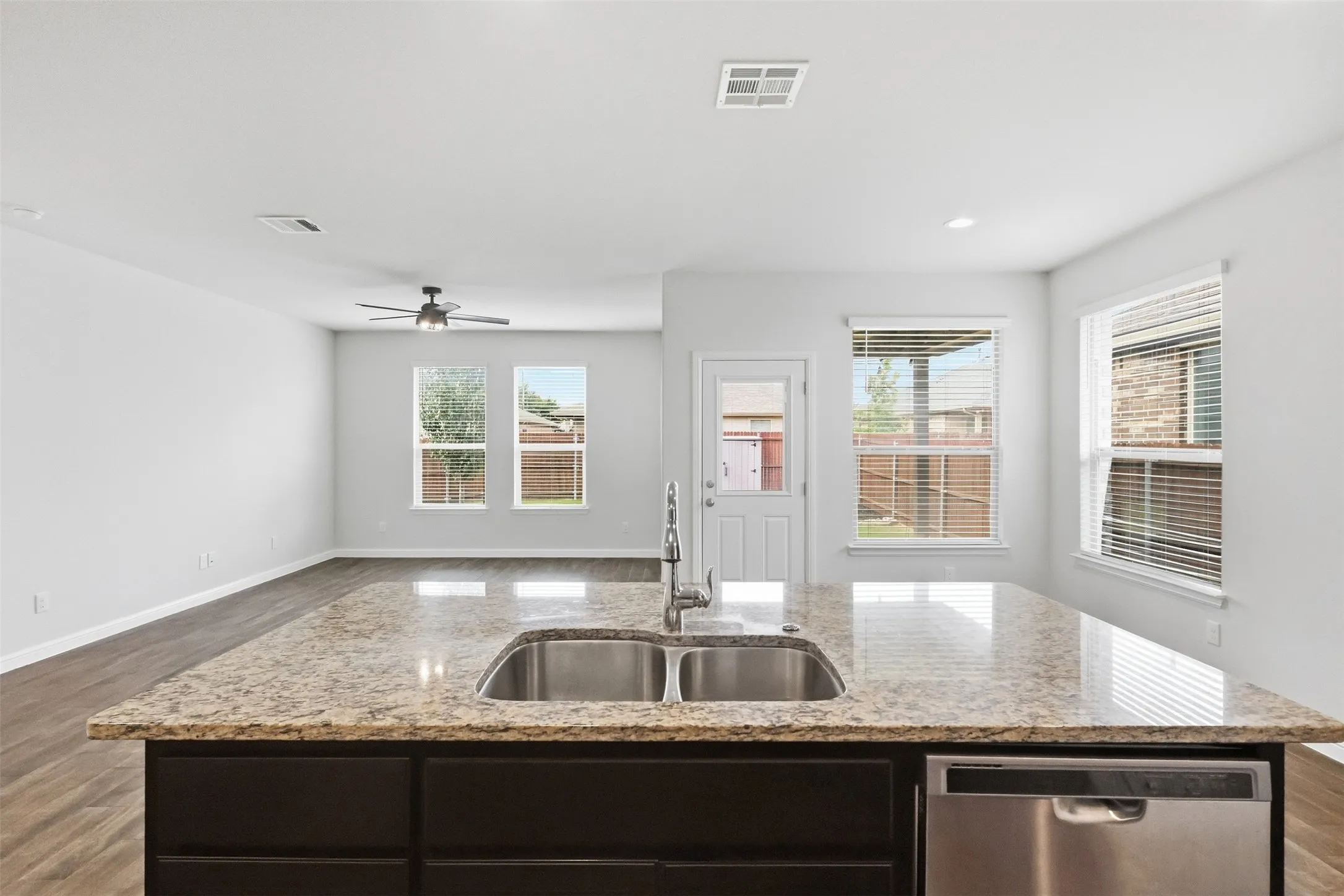 Kitchen island with a double basin stainless steel sink, granite countertop, and dark wood cabinetry