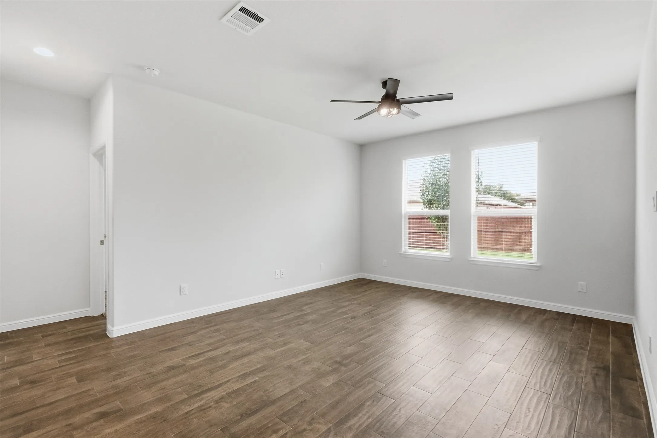 Spacious room featuring wood-finish flooring, white walls, and a ceiling fan with integrated lighting