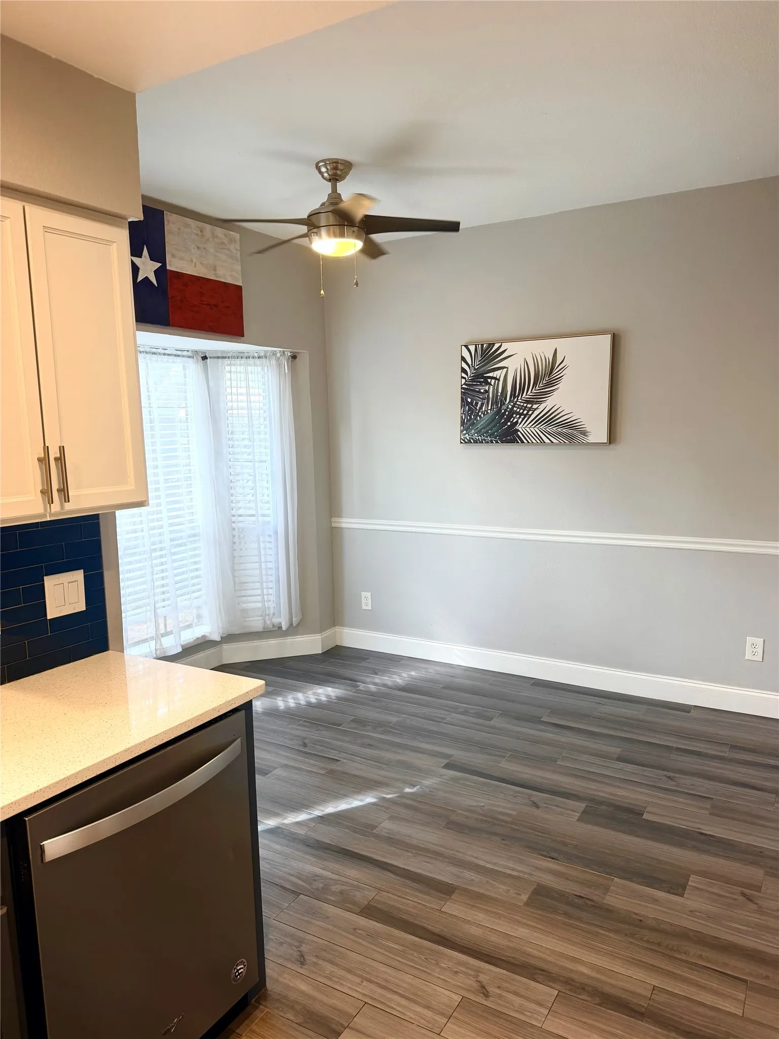 Wood-finish flooring throughout, bright window with blinds, ceiling fan with light fixture, built-in dishwasher, and white cabinetry with gold-tone hardware