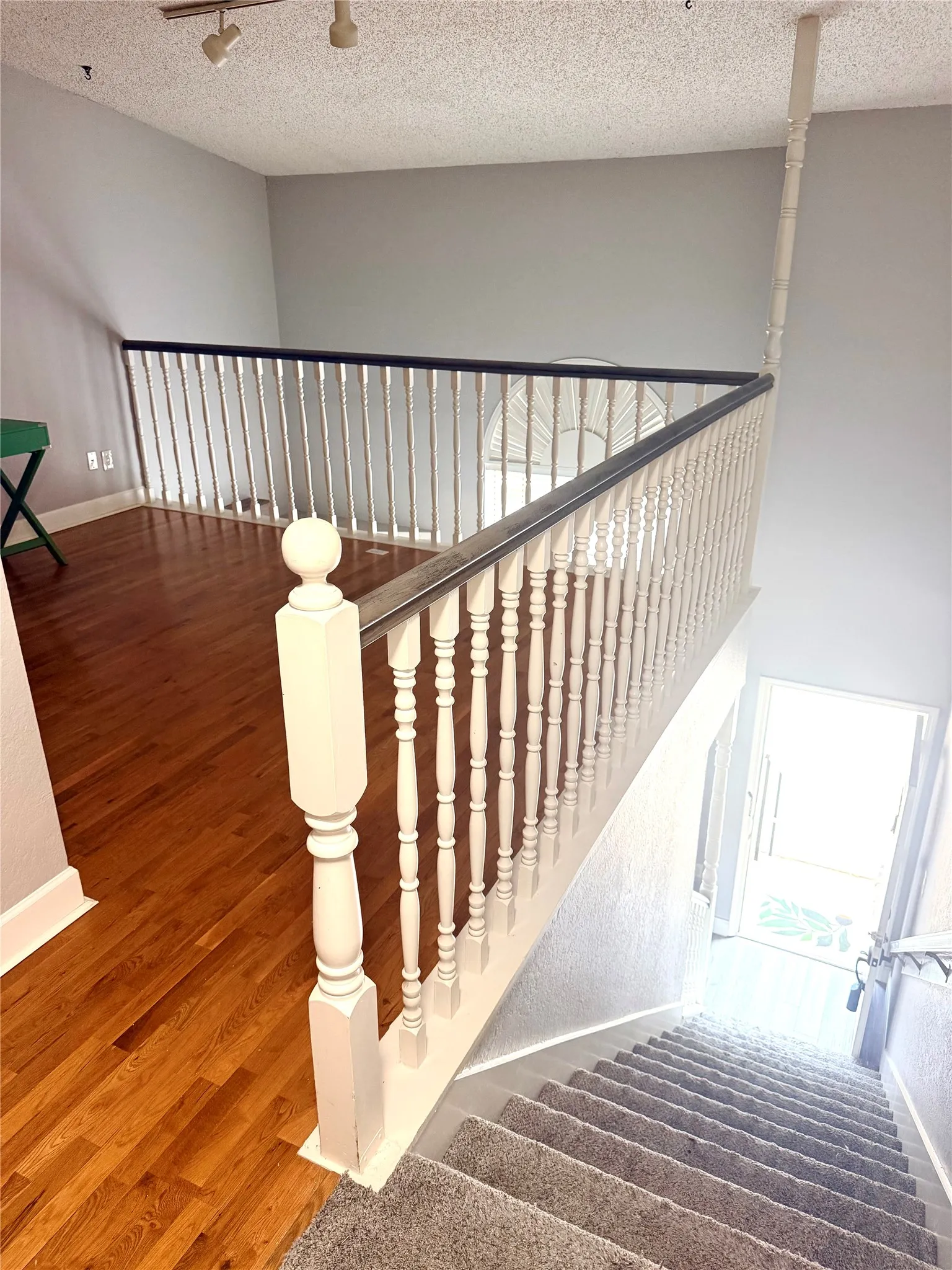 Hardwood flooring, painted banister with turned spindles, track lighting, gray wall paint, and carpeted stairs