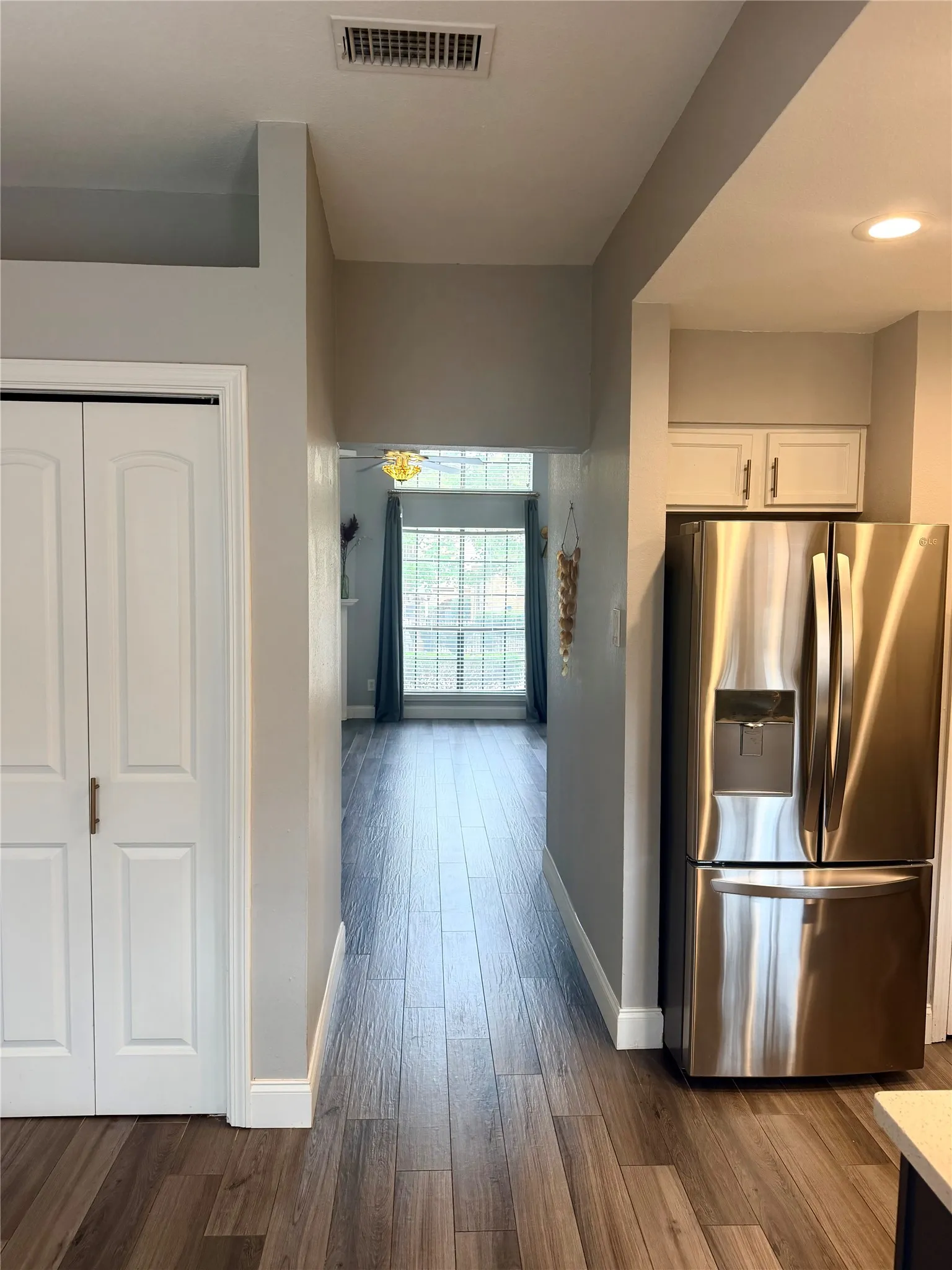 Wood-finish flooring, white bi-fold closet doors, stainless steel refrigerator, white upper cabinetry, and recessed lighting