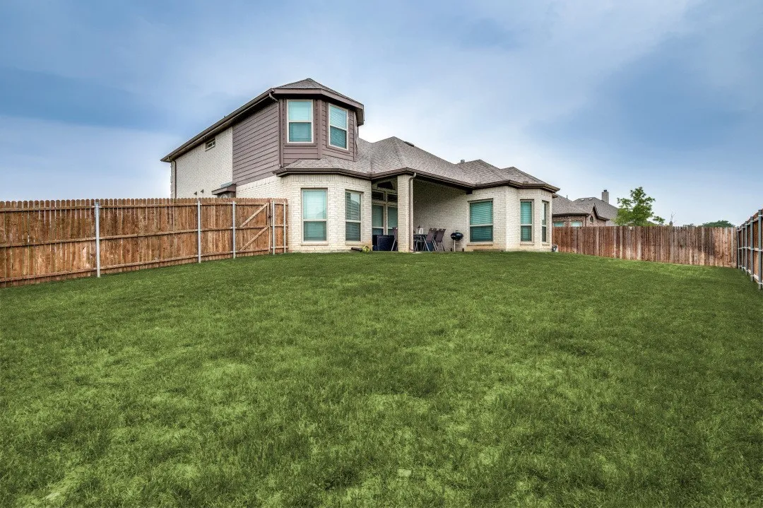 Spacious backyard with a privacy fence, covered patio, and large lawn