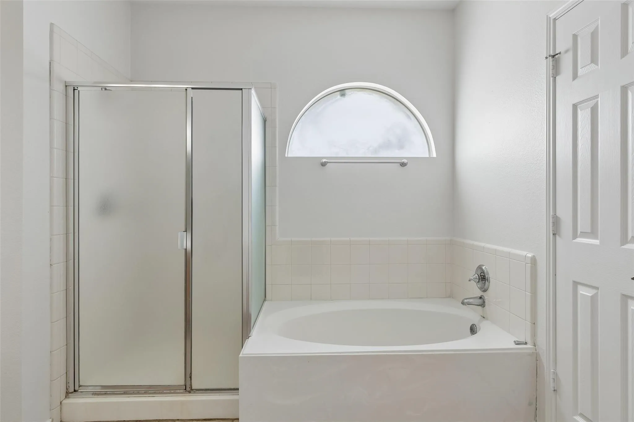 Built-in soaking tub with chrome fixtures, tiled surround, and frosted arch window