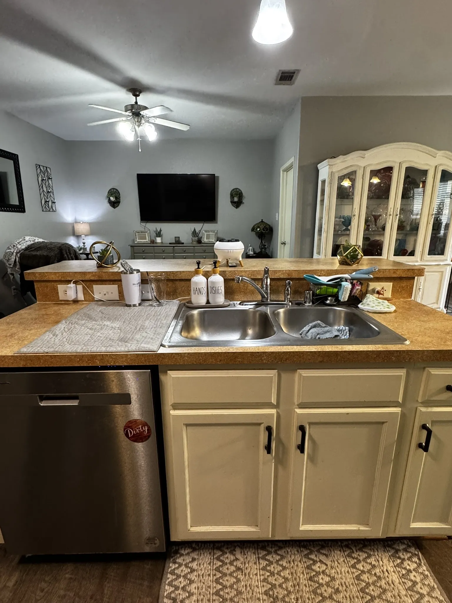 Kitchen featuring a stainless steel double basin sink, light-toned countertops, painted cabinetry with dark hardware, and a stainless steel dishwasher