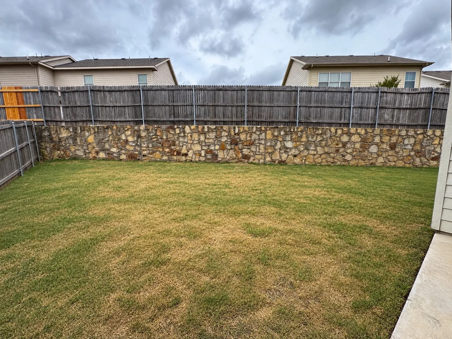 Expansive backyard featuring a stone retaining wall and a wood privacy fence 1