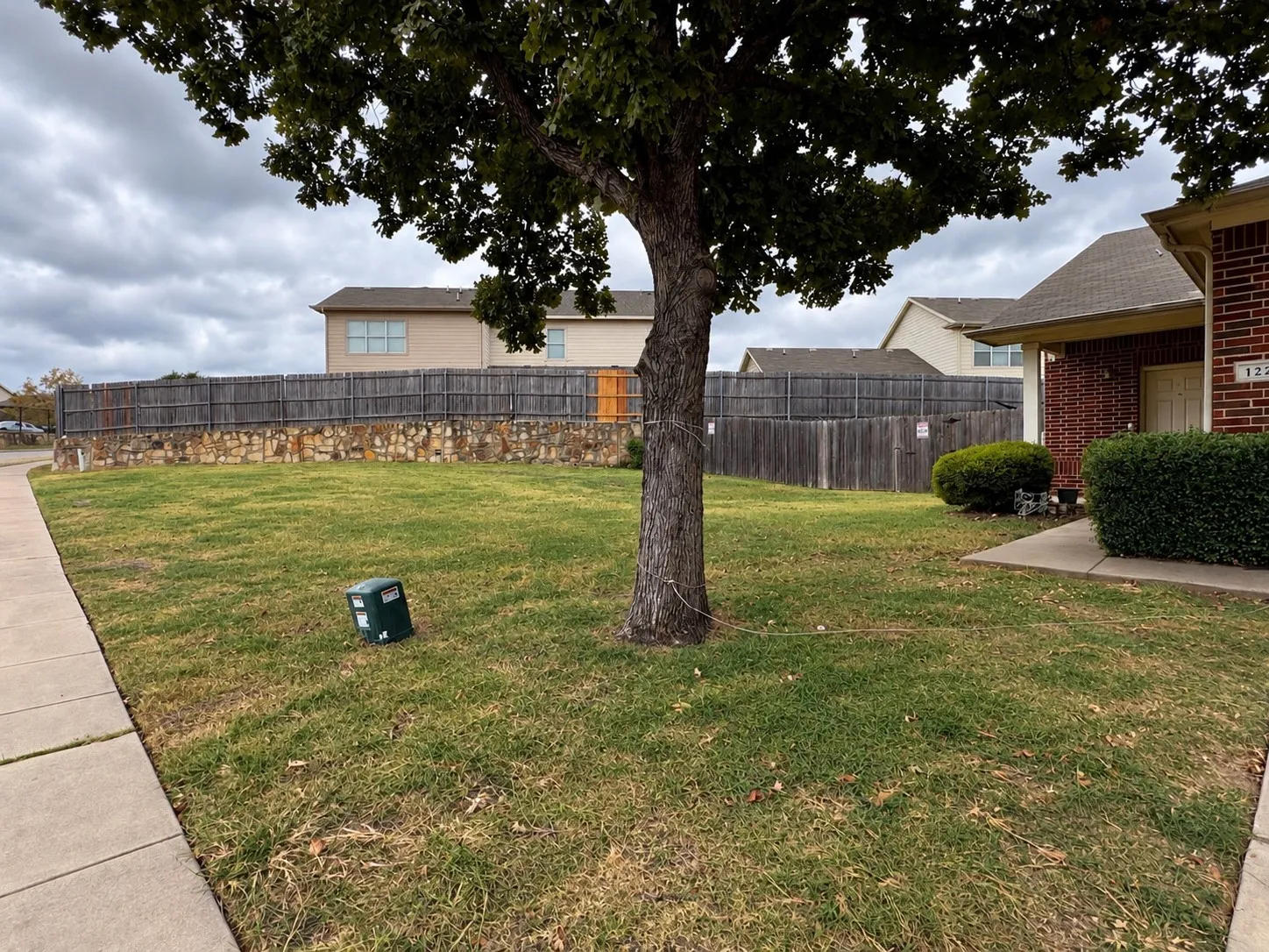 Manicured front lawn with mature tree, concrete sidewalk, and a brick exterior facade