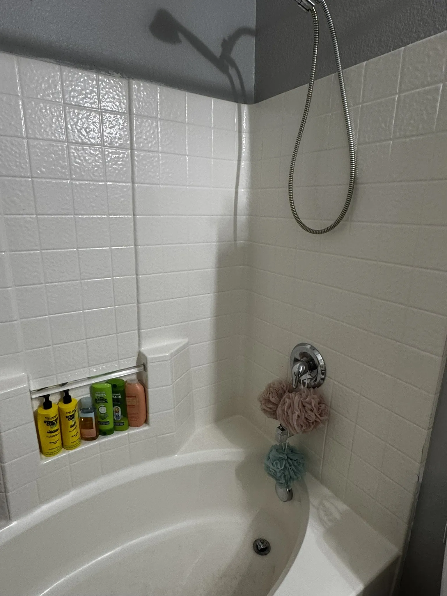 Bathtub featuring a built-in shower niche, chrome fixtures, and white tiled surround
