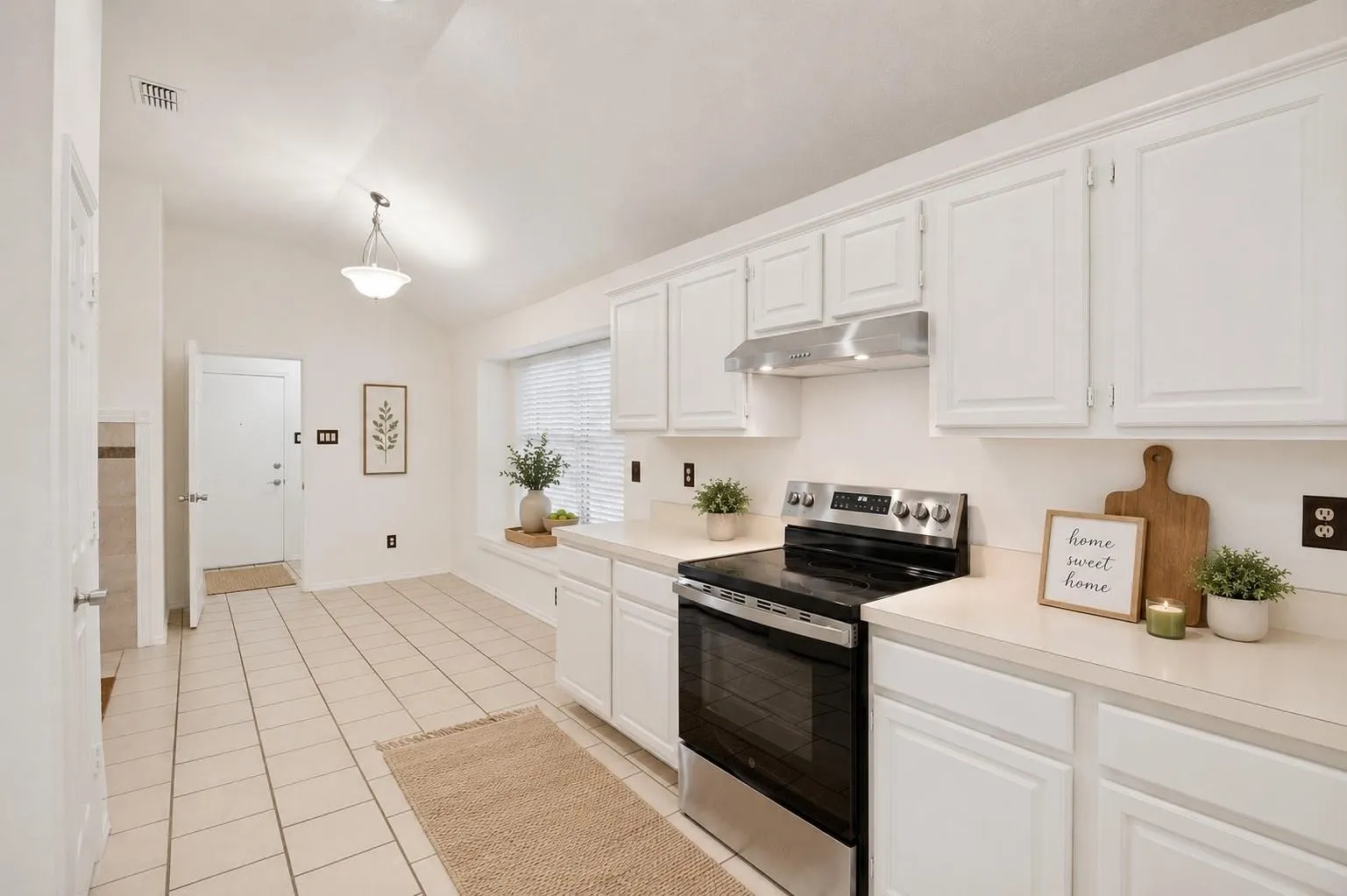 White cabinetry, stainless steel range with overhead ventilation, light-toned countertops, and tile flooring