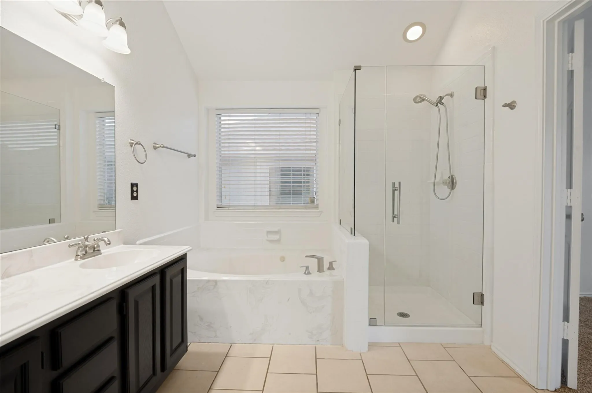 Tile flooring, dark wood-finish vanity with white countertop, recessed lighting, built-in bathtub, and glass-enclosed shower