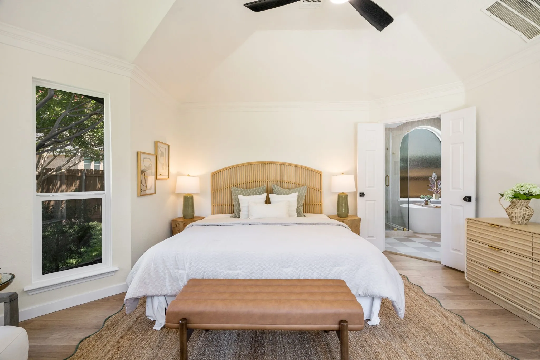 Vaulted ceiling with crown molding, wood-finish flooring, tall window, and dual French doors opening to a bathroom with a freestanding tub